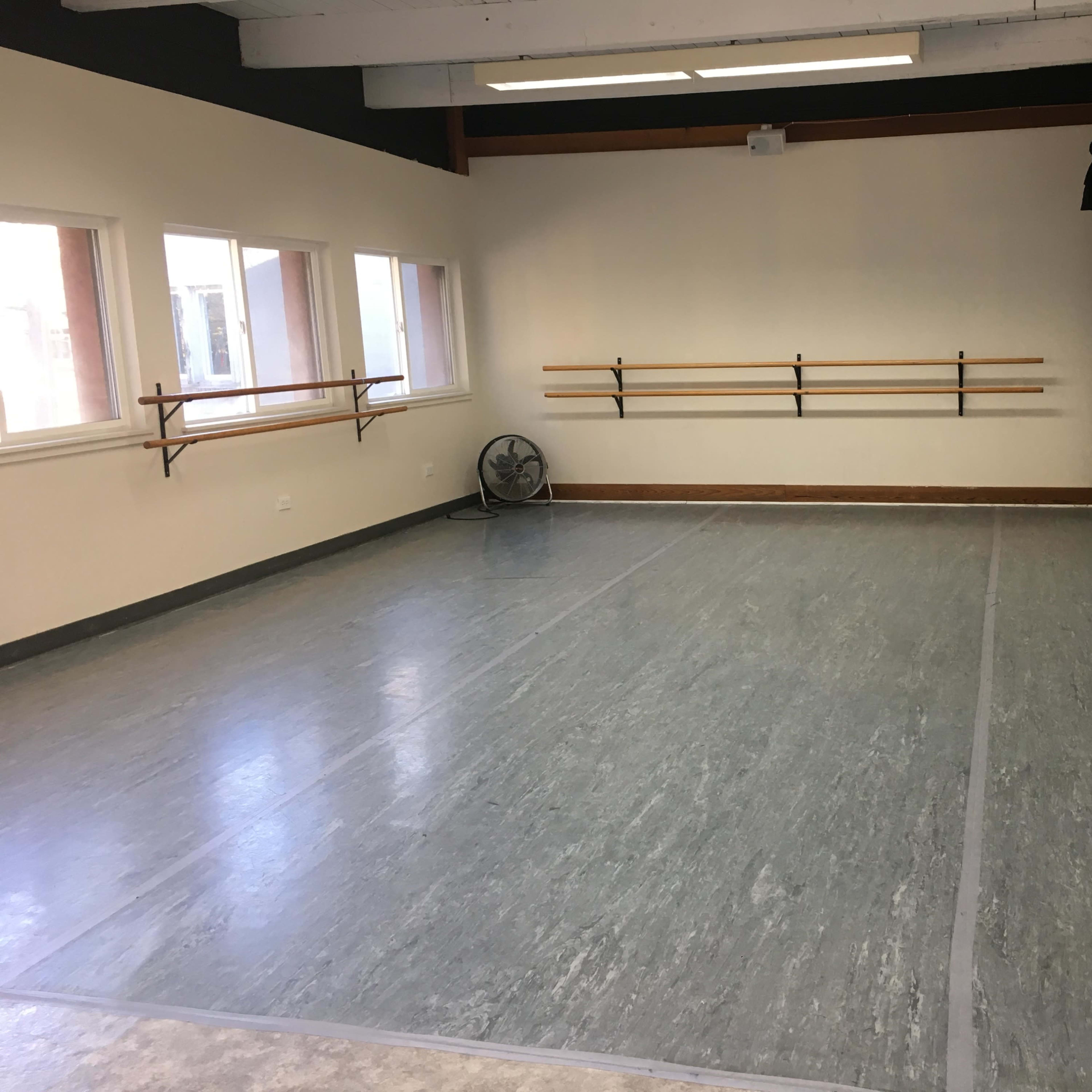 An empty dance studio with wooden ballet bars mounted on the wall and a large mirror along one side.
