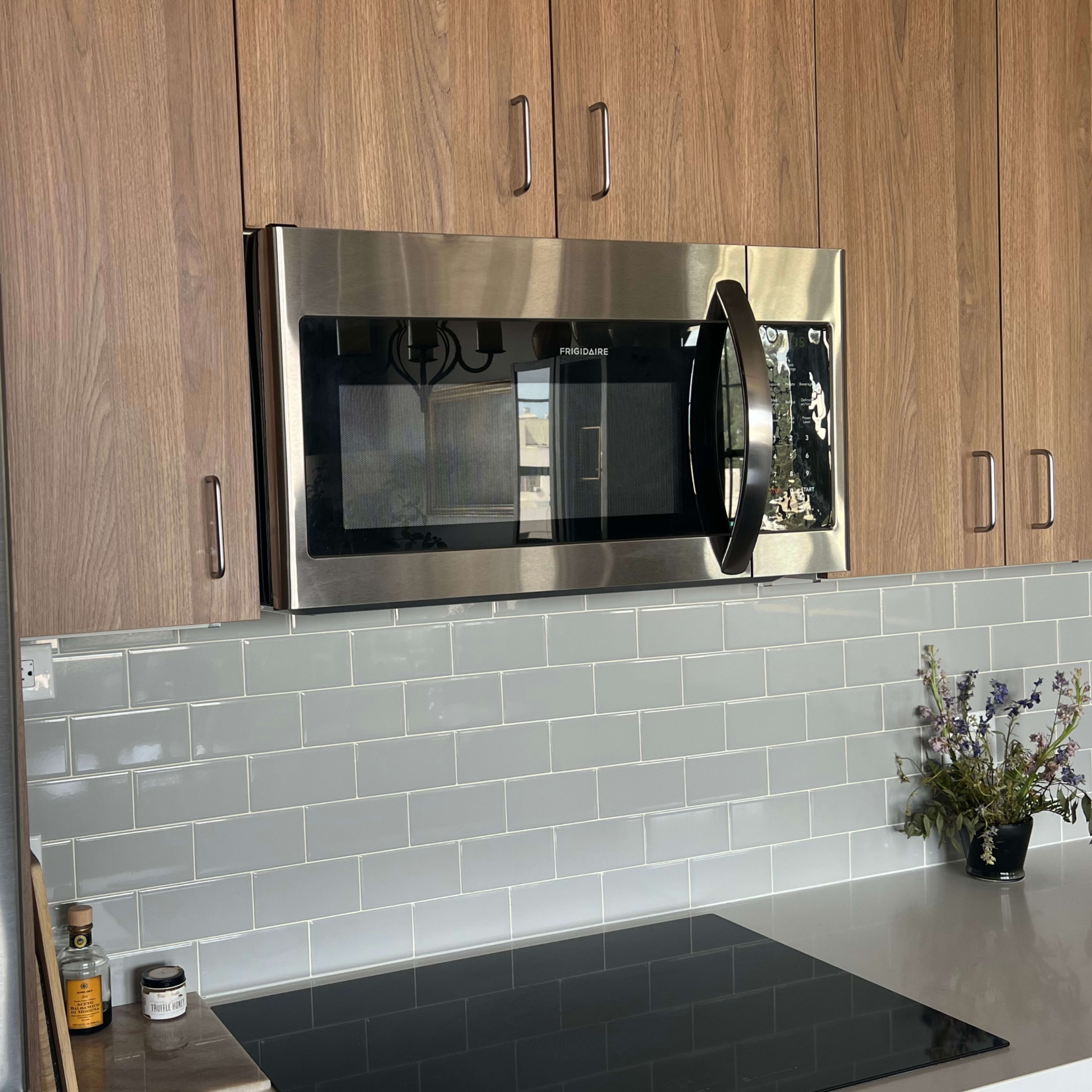 A modern kitchen with a stainless steel refrigerator, a microwave mounted above the countertop, and a glass tile backsplash.