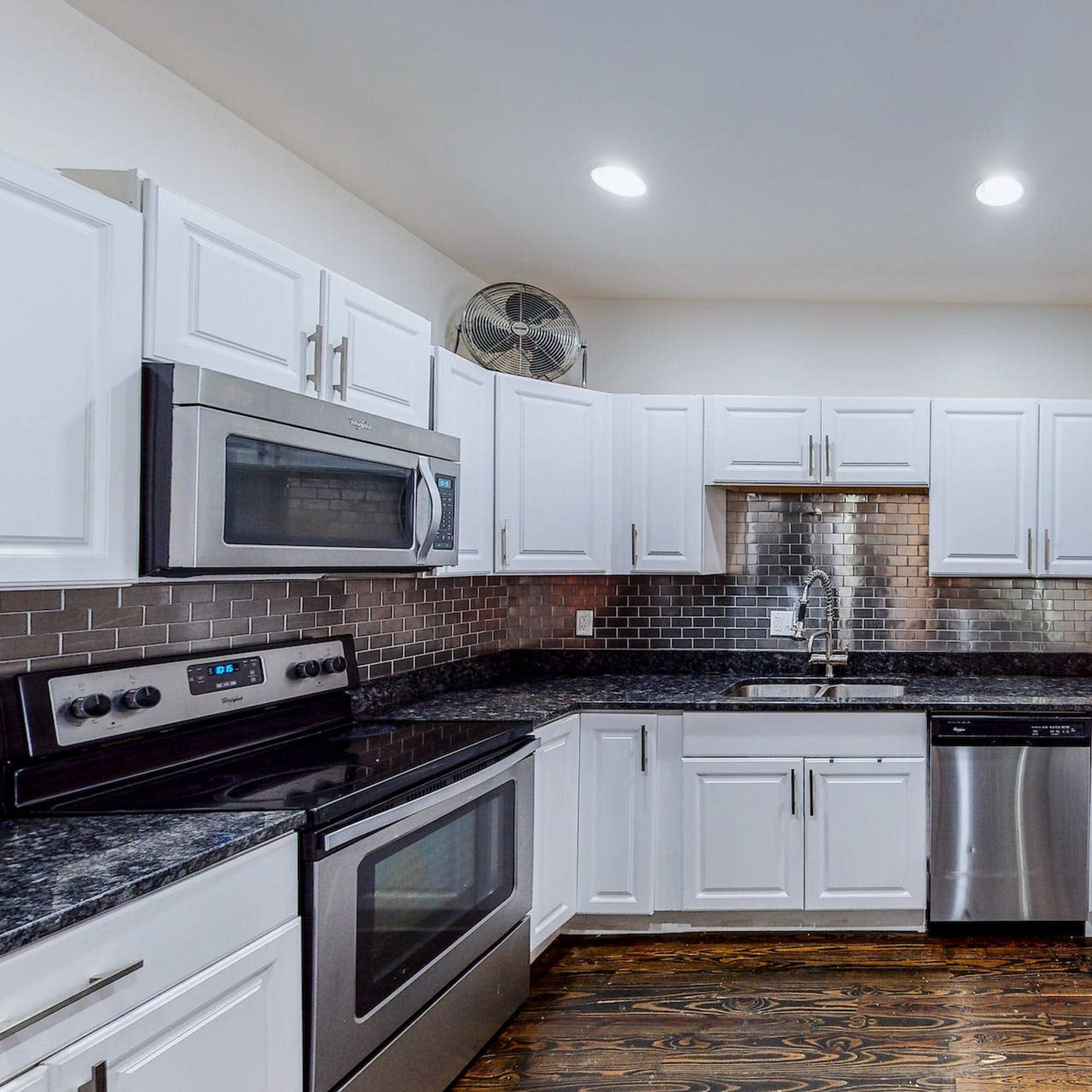 A modern kitchen with white cabinets, stainless steel appliances, and dark granite countertops.
