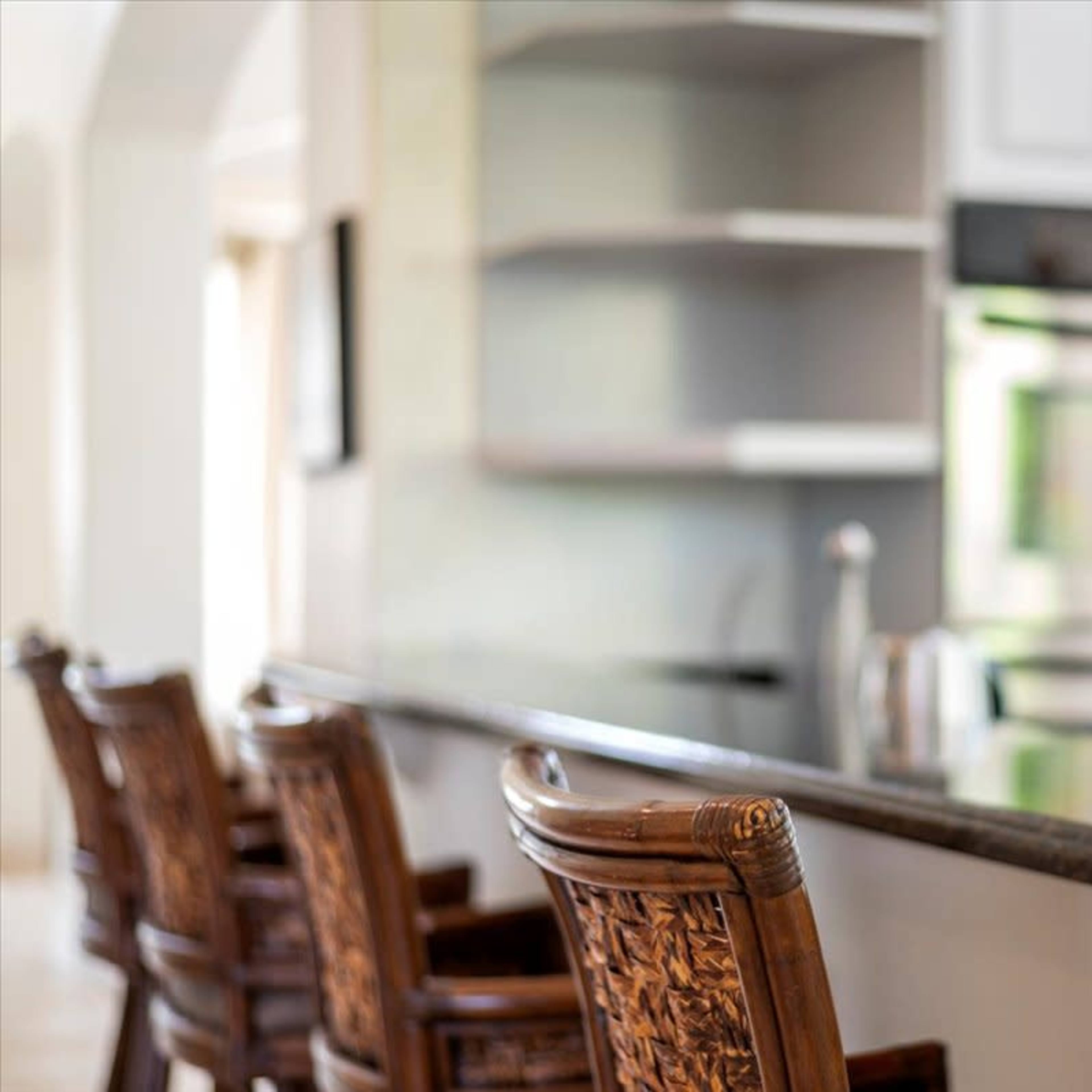 A kitchen bar with four wooden chairs and stainless steel appliances in the background.