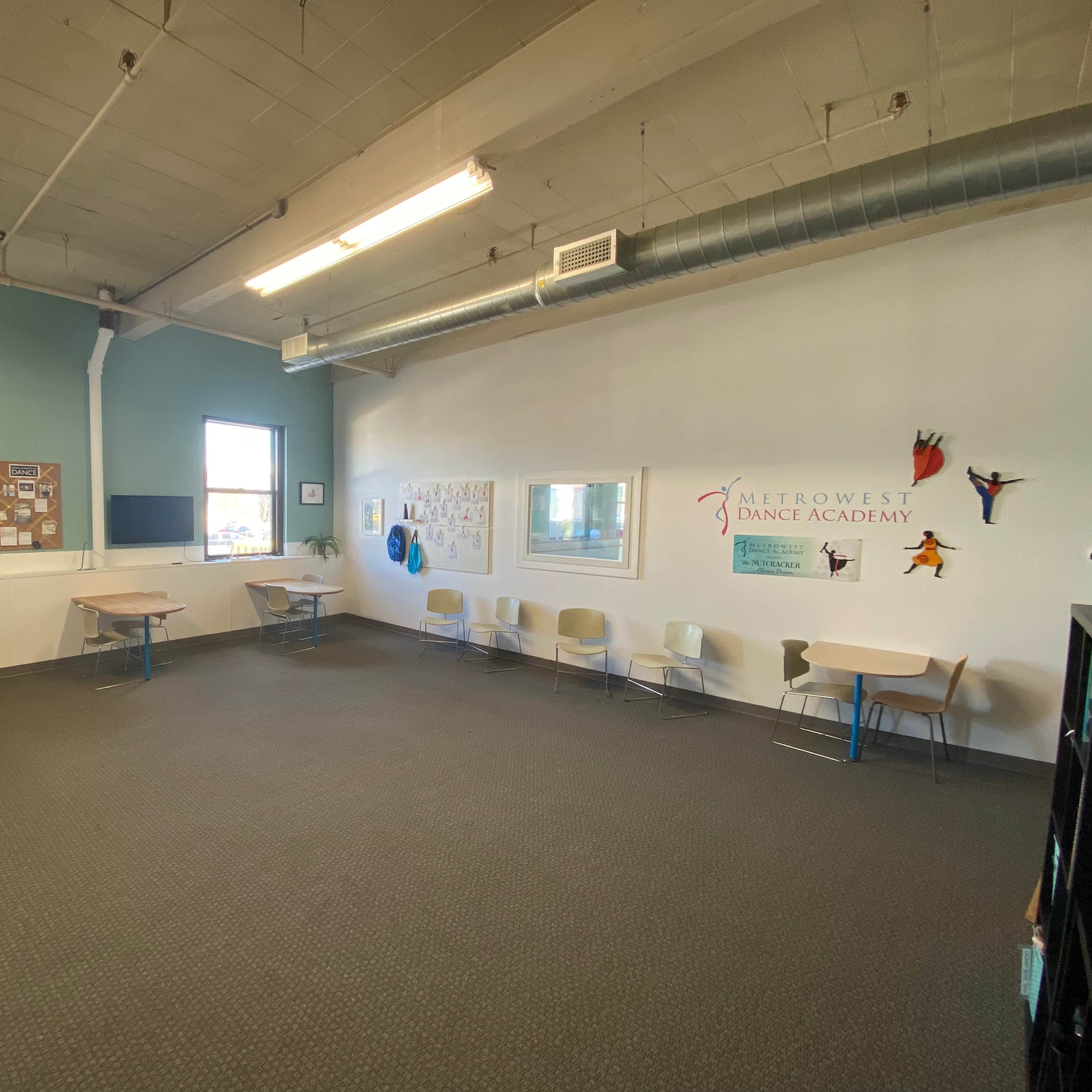 A spacious, well-lit dance studio with several tables and chairs arranged along the walls.