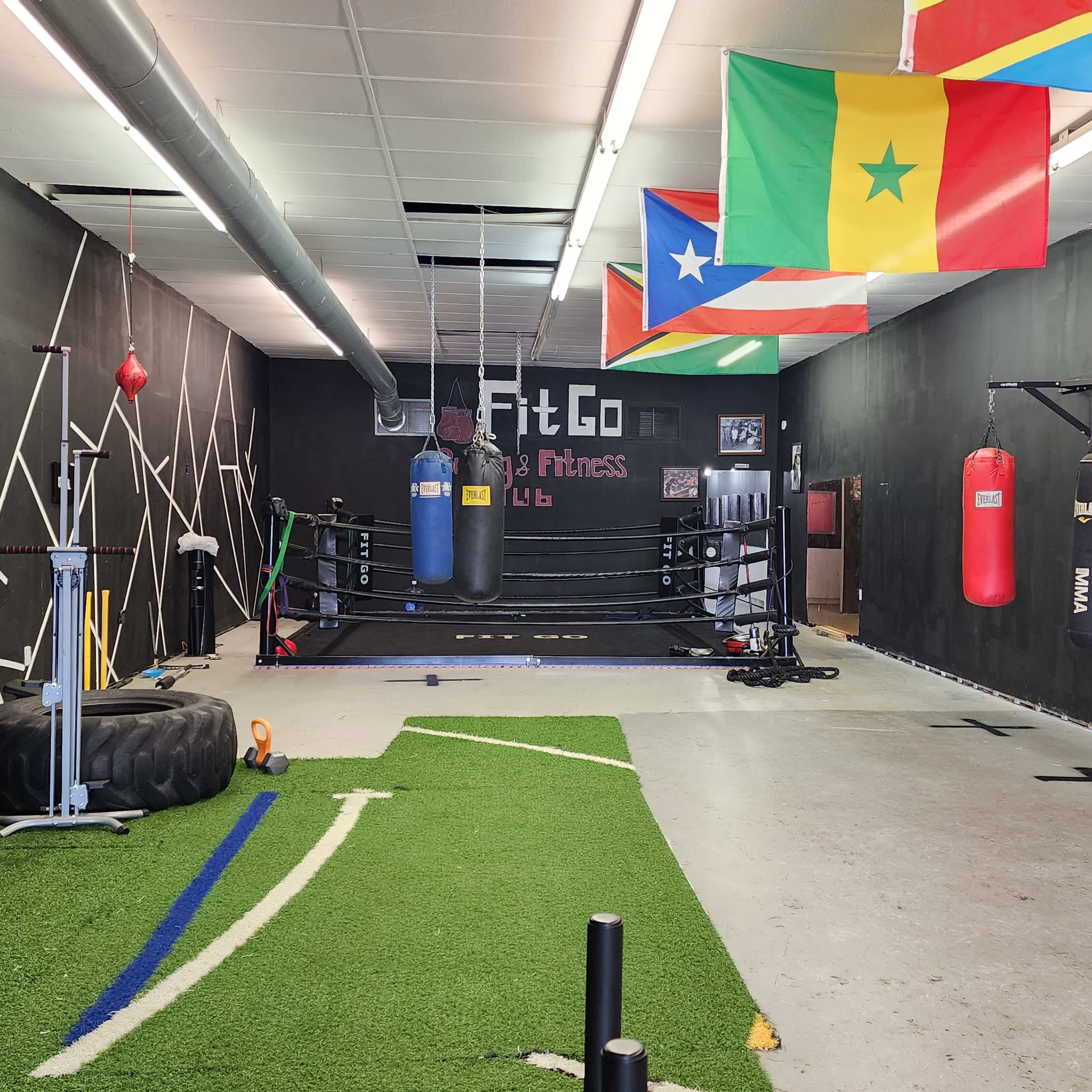 An indoor fitness area with a boxing ring, punching bags, exercise equipment, and various flags hanging on the walls.