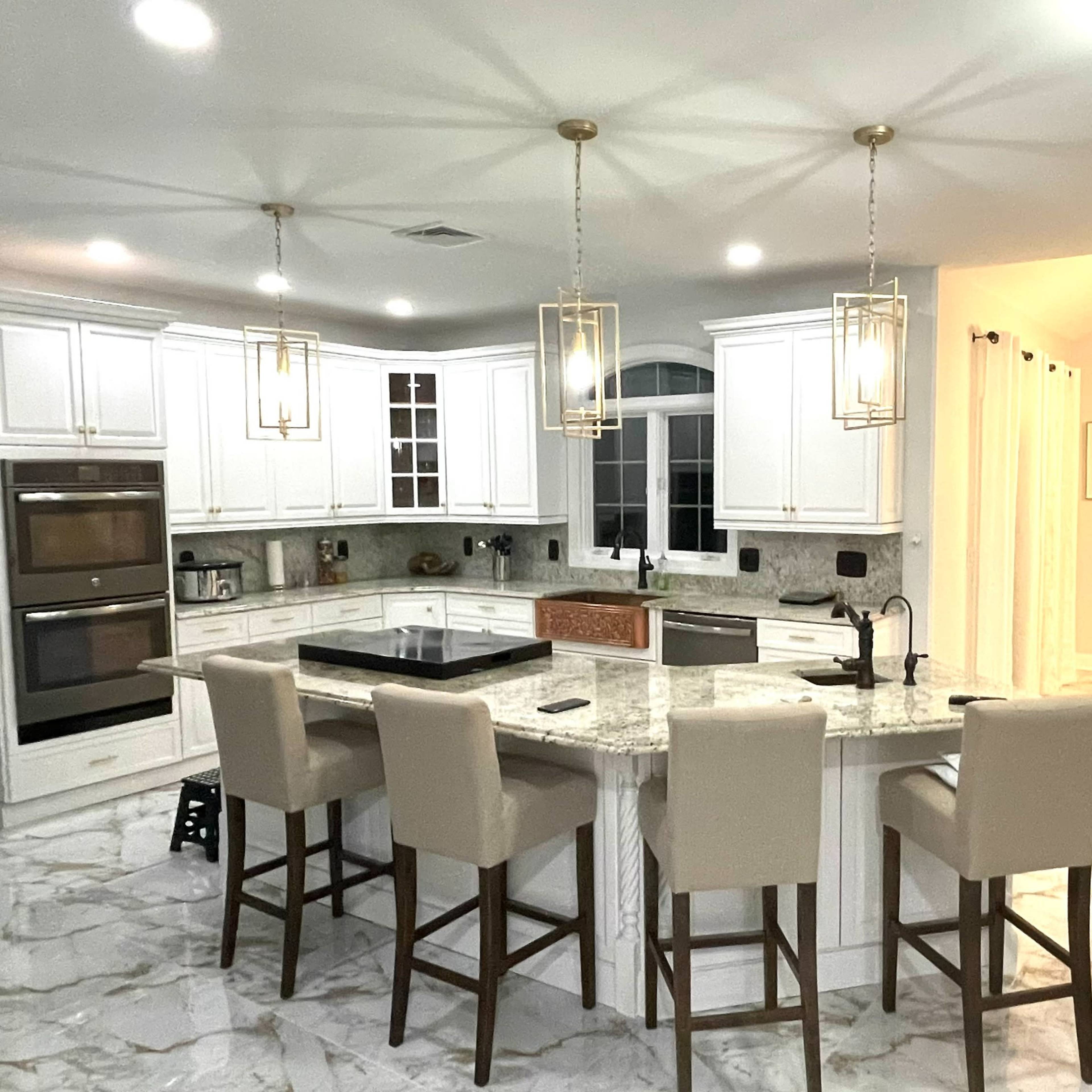 A modern kitchen features white cabinetry, marble countertops, and a large island with bar seating, adjacent to a dining area with a table and chairs.