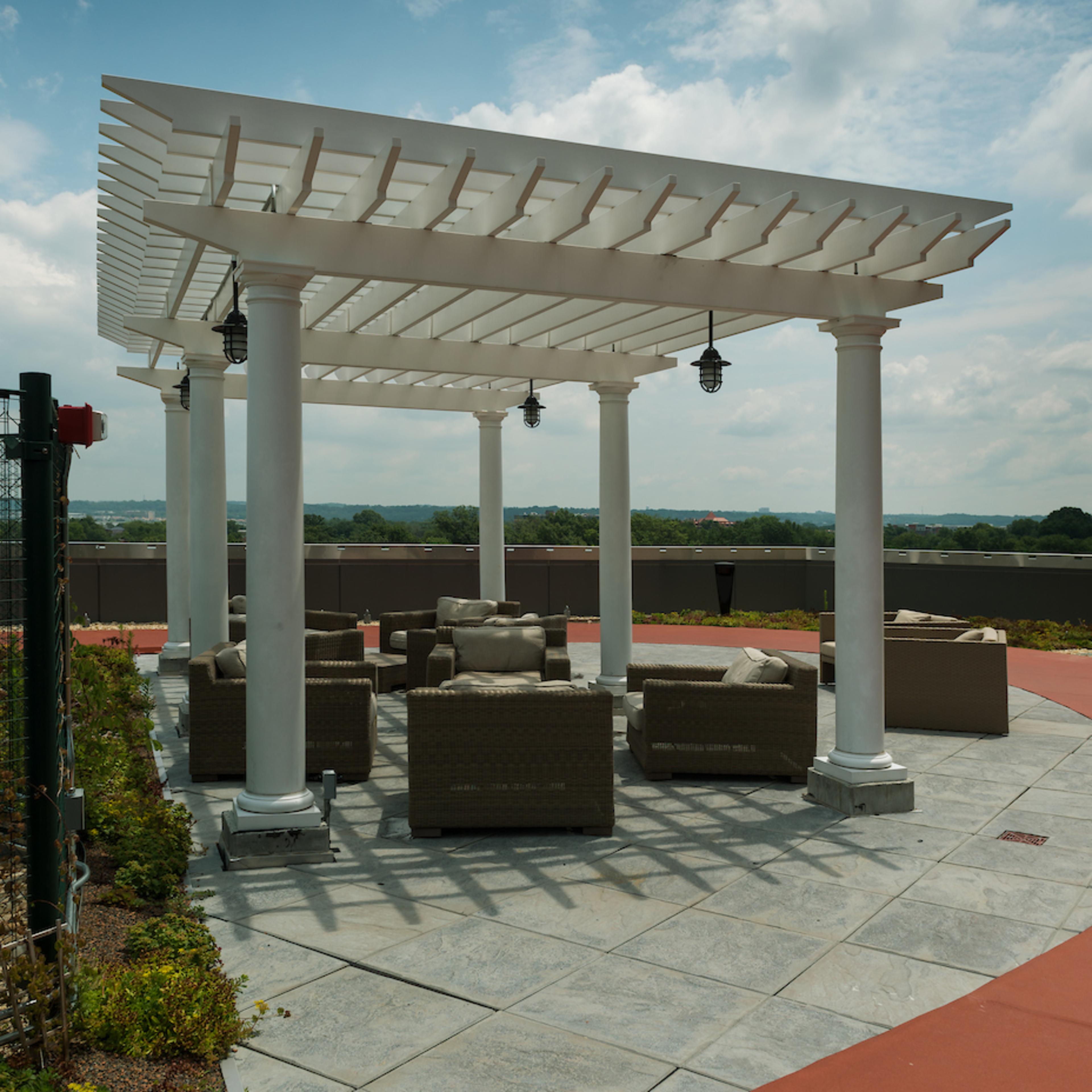 A white pergola with hanging lamps shades a seating area of wicker chairs and tables on a stone patio.