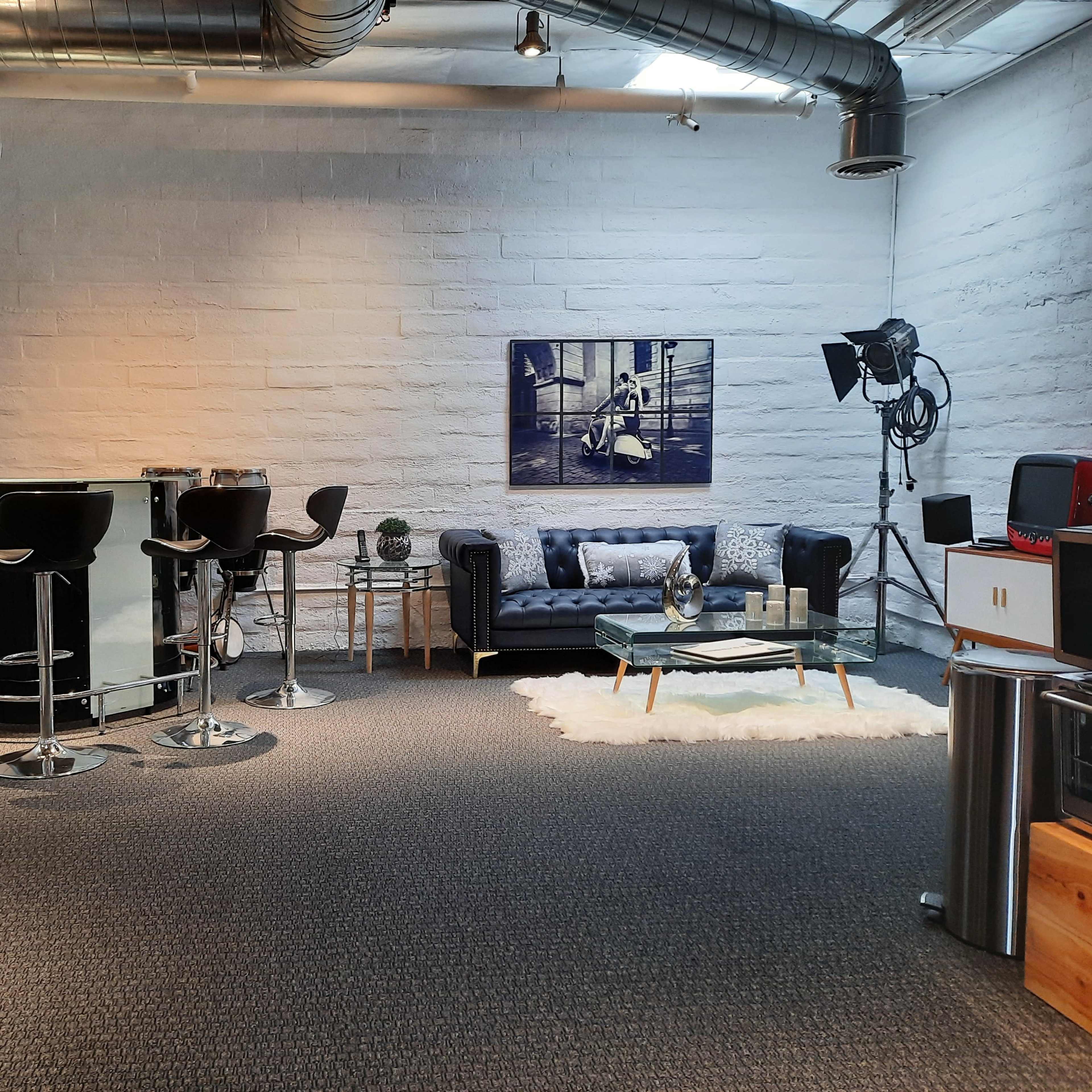 A modern indoor space featuring a blue couch, bar-style seating, a coffee table, and a large light fixture against a light gray wall.