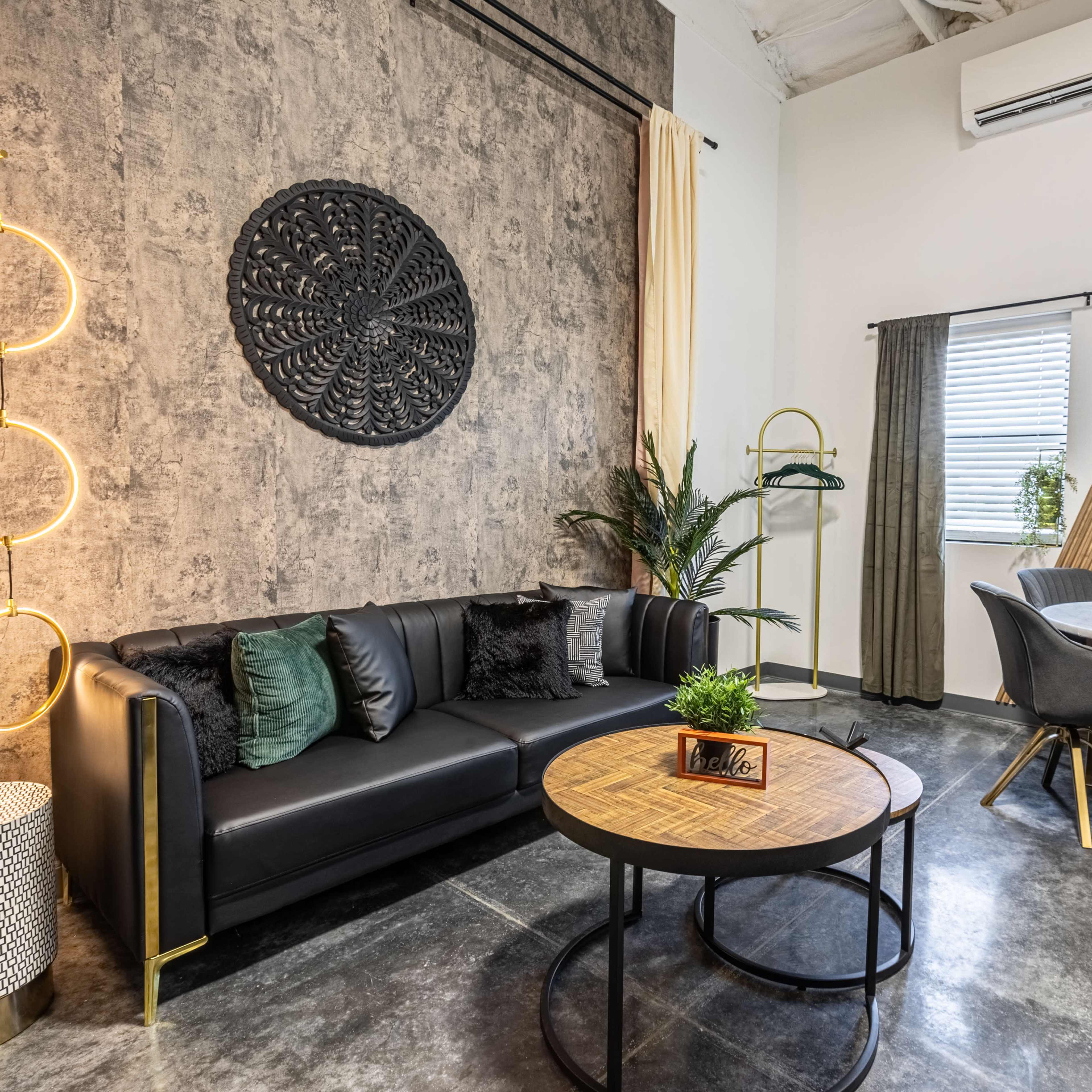 A modern living space featuring a black leather sofa, a round wooden coffee table, and a dining area with stylish chairs and decorative plants.
