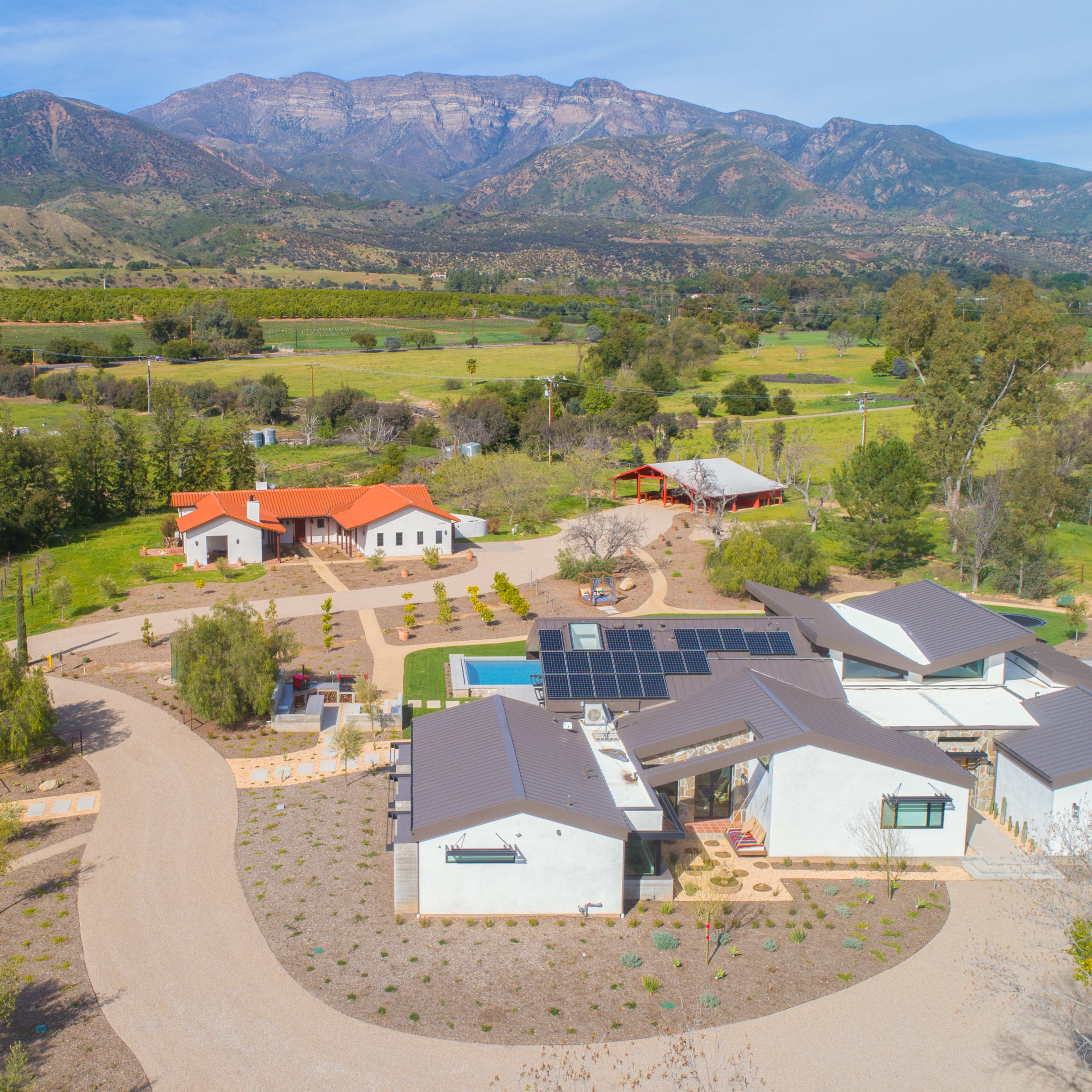 A sprawling rural property featuring multiple structures, a swimming pool, solar panels, and mountainous terrain in the background.