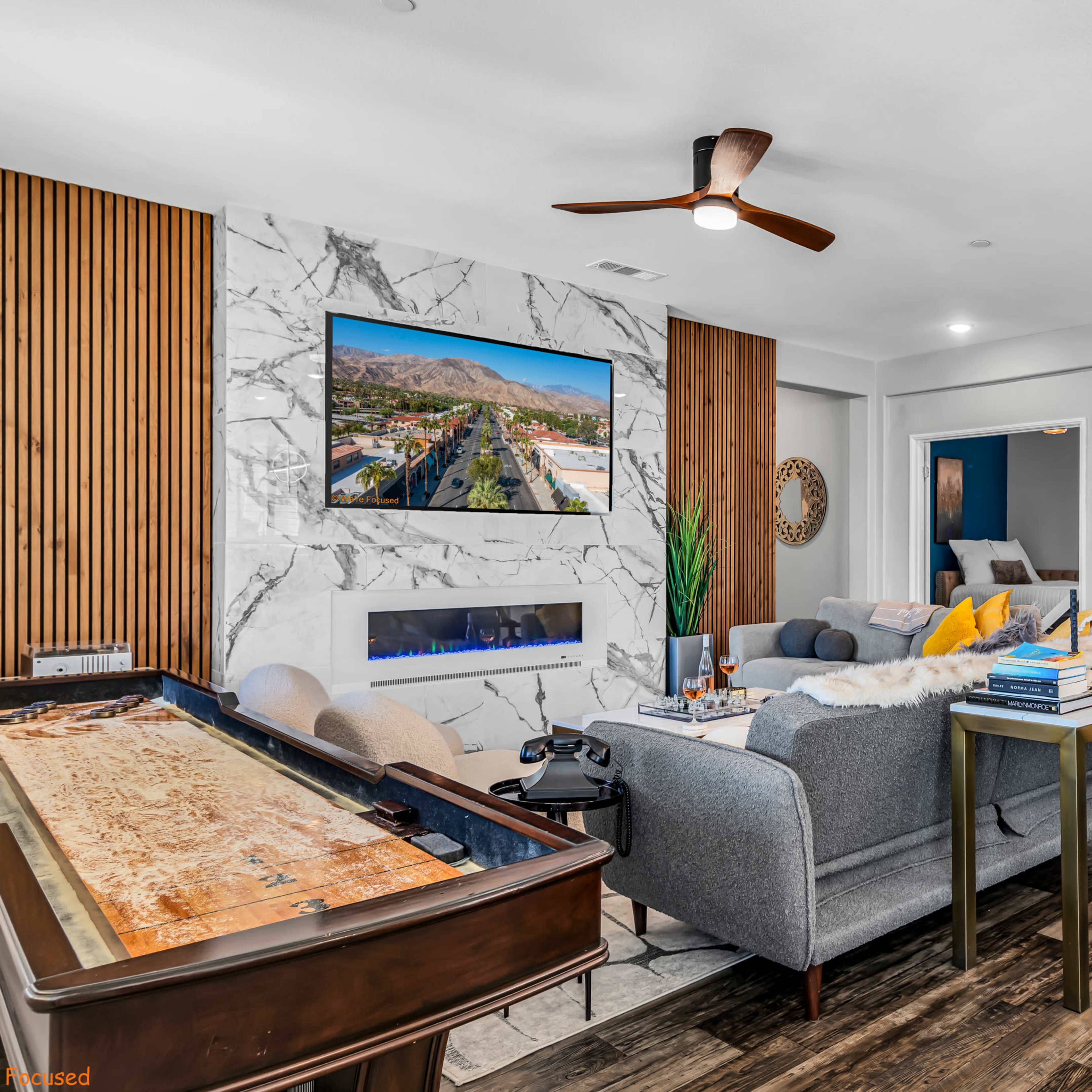 The living room features a marble accent wall, a ceiling fan, a large television mounted above a modern fireplace, and a sectional sofa with various decorative pillows.