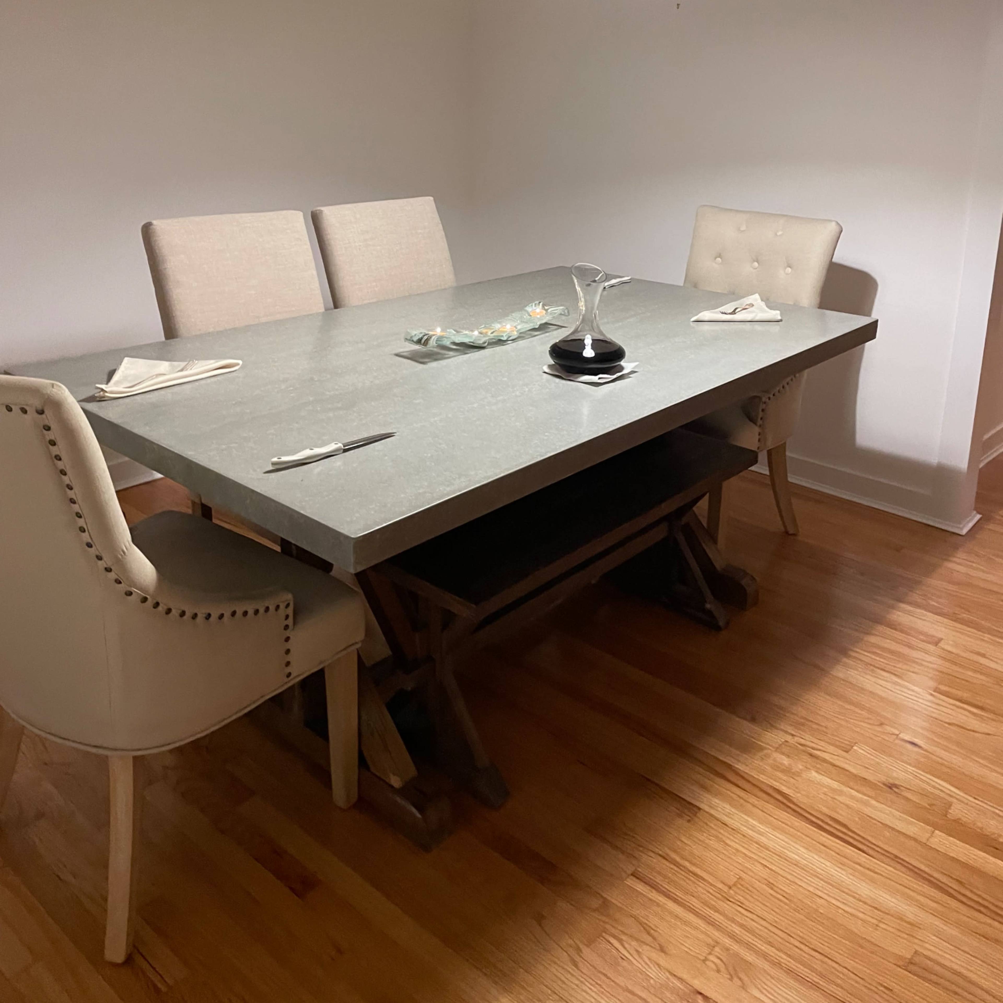 A minimalist dining area features a large gray table with four chairs and a pendant light hanging above.