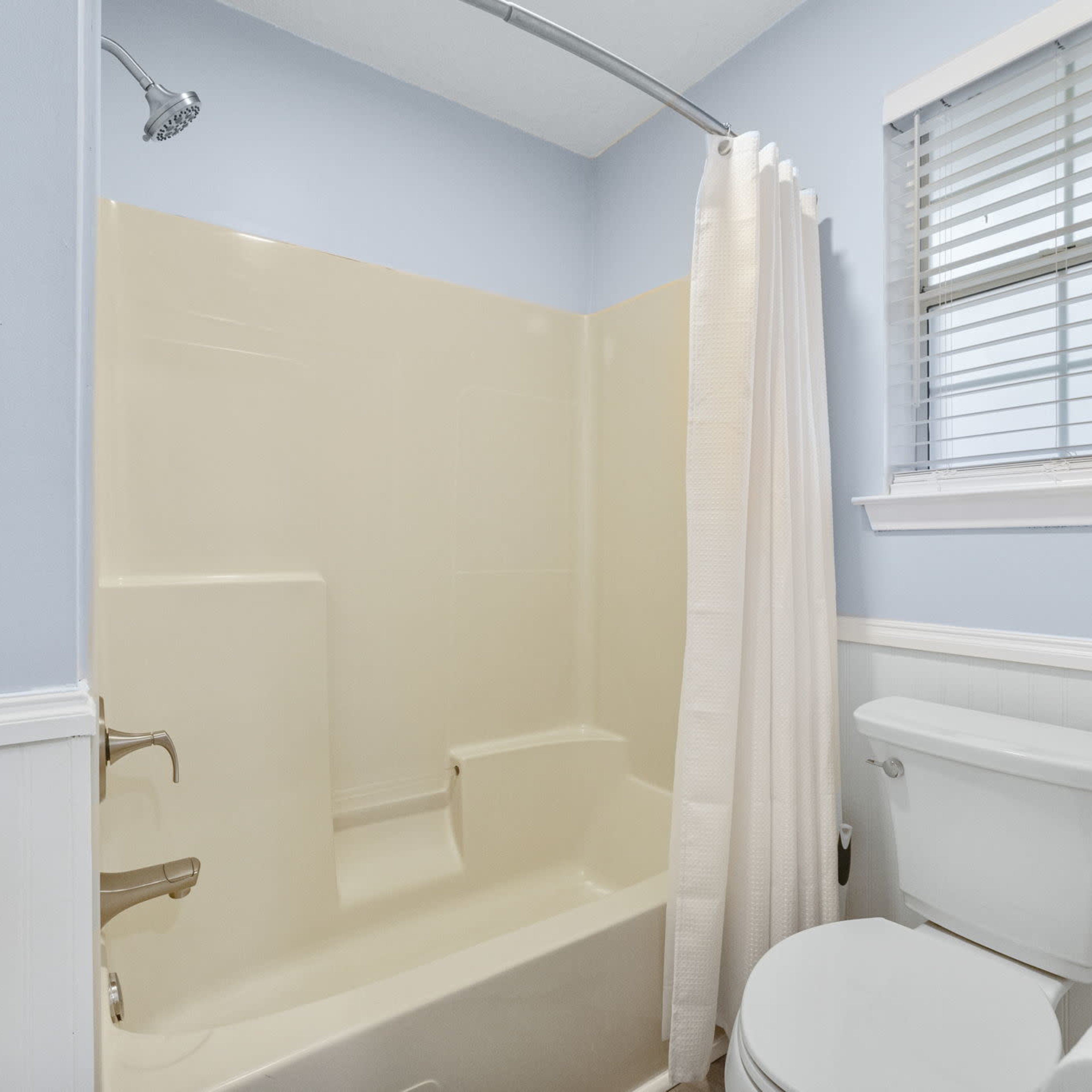 A bathroom featuring a shower-tub combination, a toilet, and light blue walls with white trim.