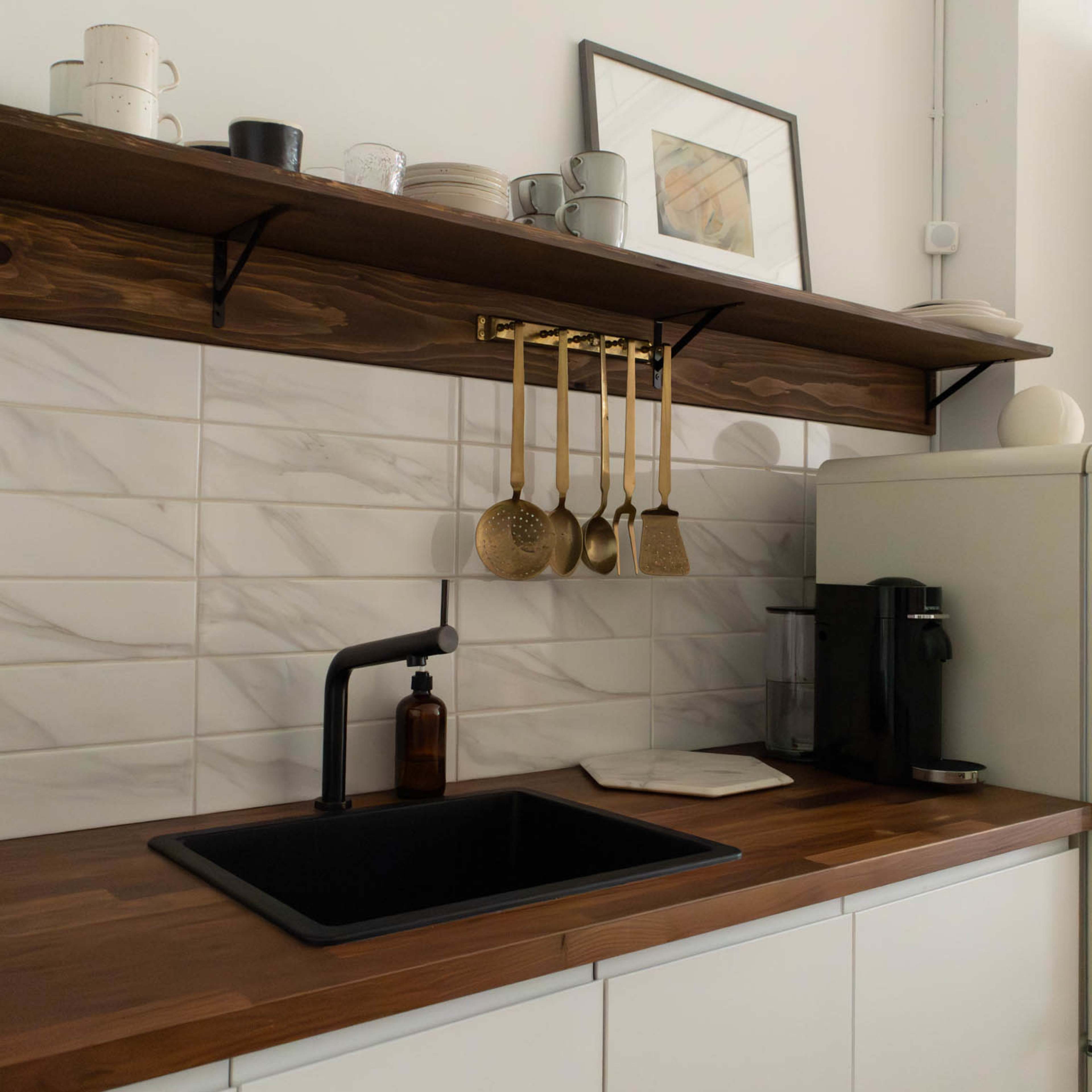 A modern kitchen features a wooden countertop with a black sink, hanging utensils, and minimalist decor on open shelves.