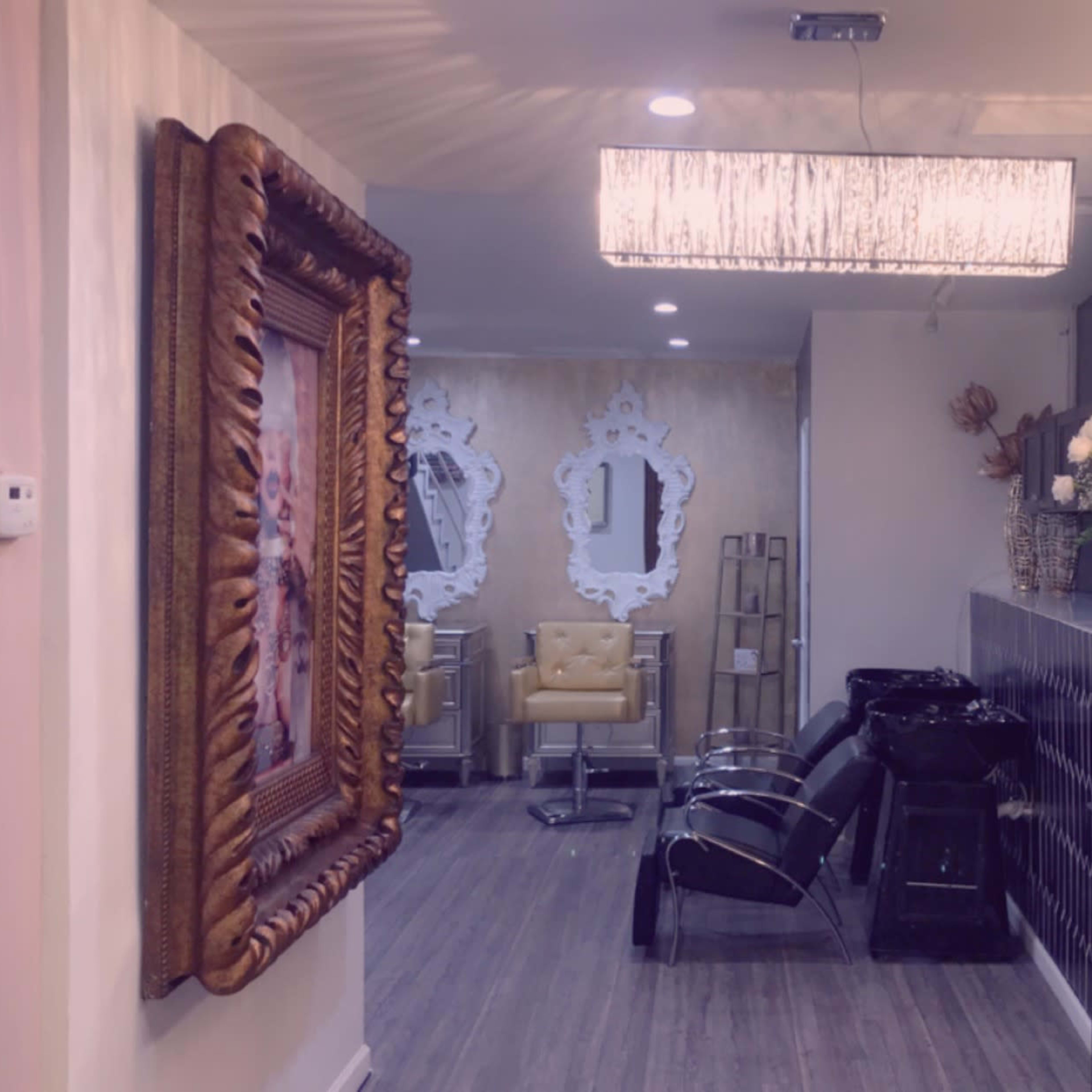 A corridor in a salon featuring a large decorative mirror, hair-washing stations, and stylish chairs, with floral arrangements and ambient lighting.