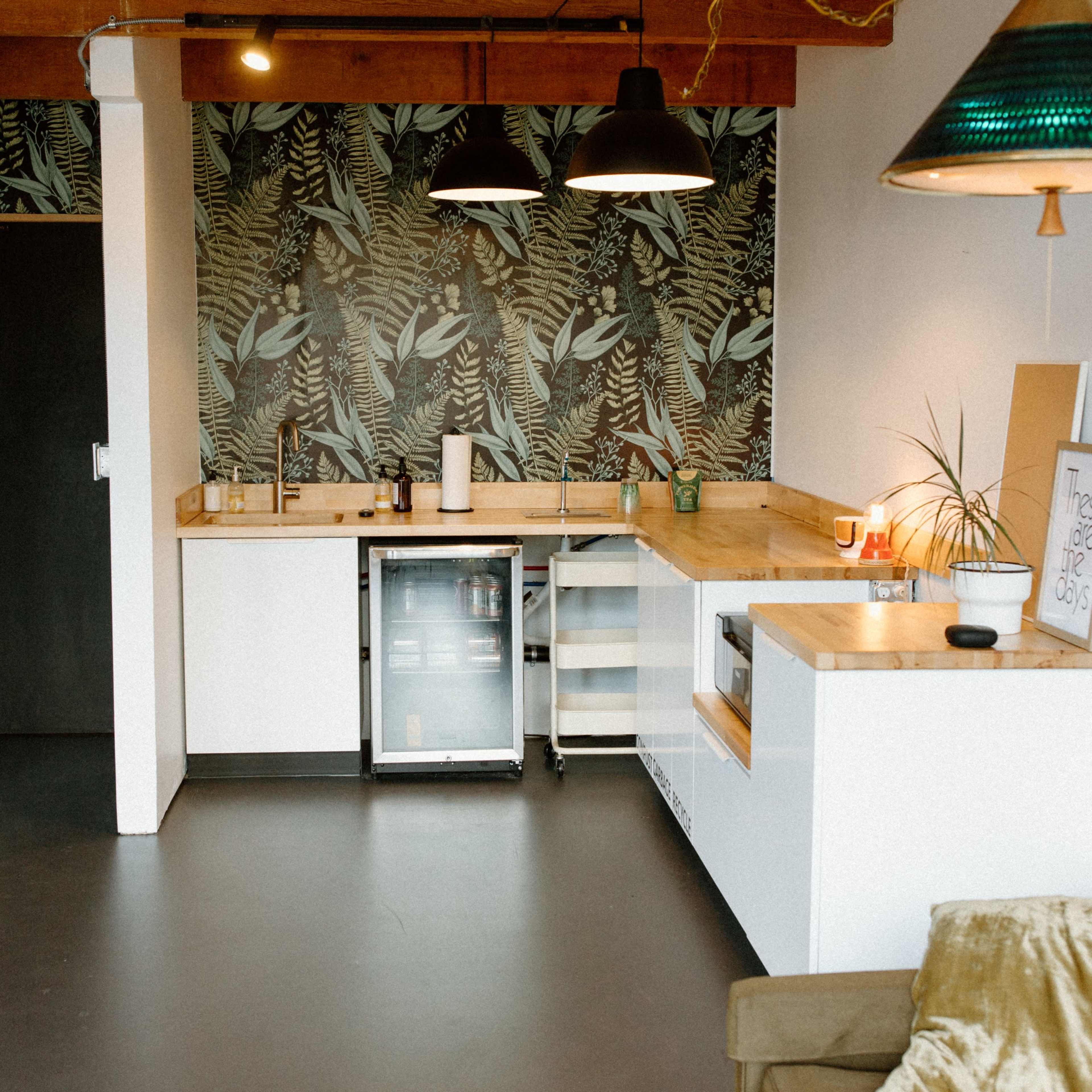A kitchen area featuring a wooden countertop, modern fixtures, a small refrigerator, and a tropical-themed wallpaper.