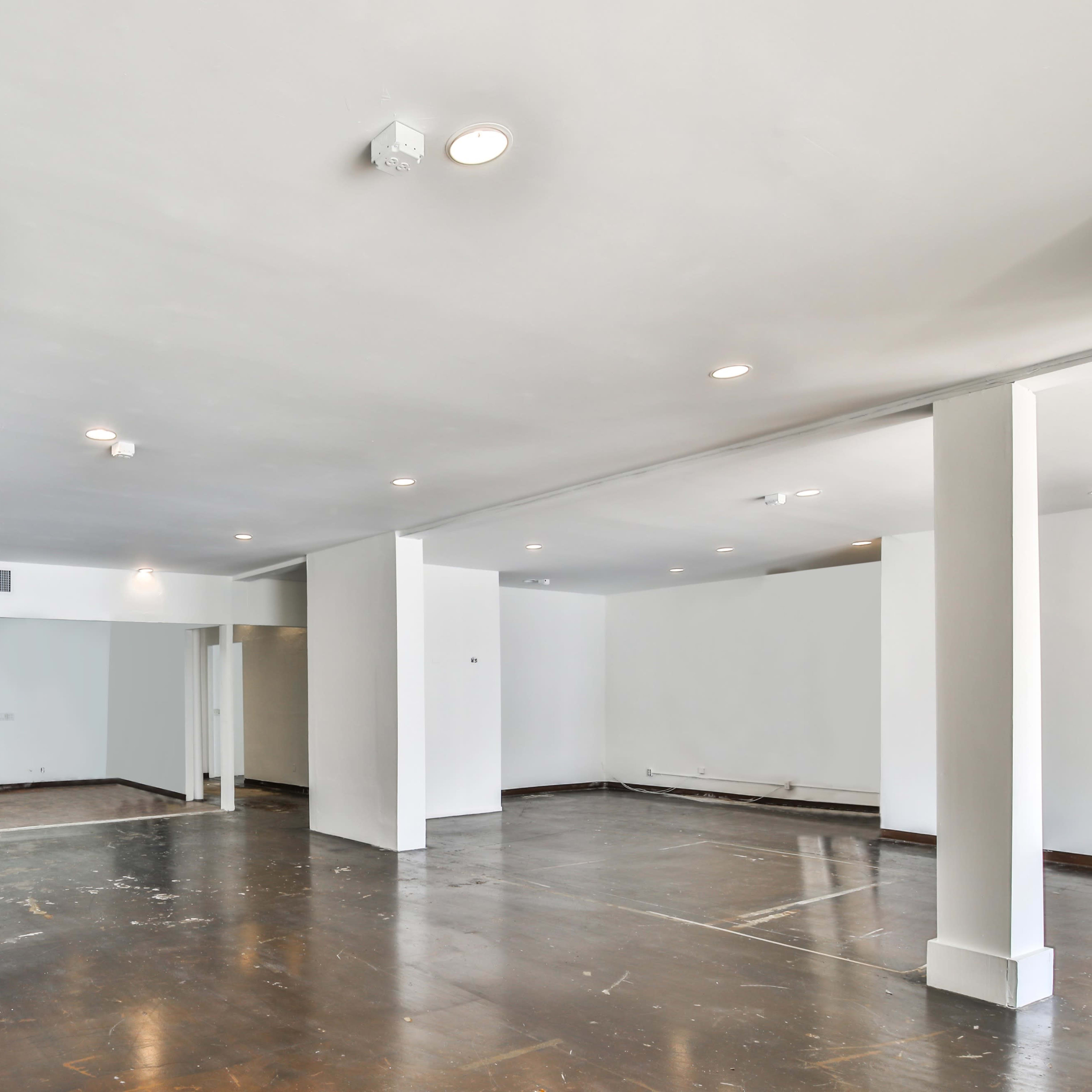 A large, empty room with a polished dark floor and white walls, illuminated by recessed ceiling lights.