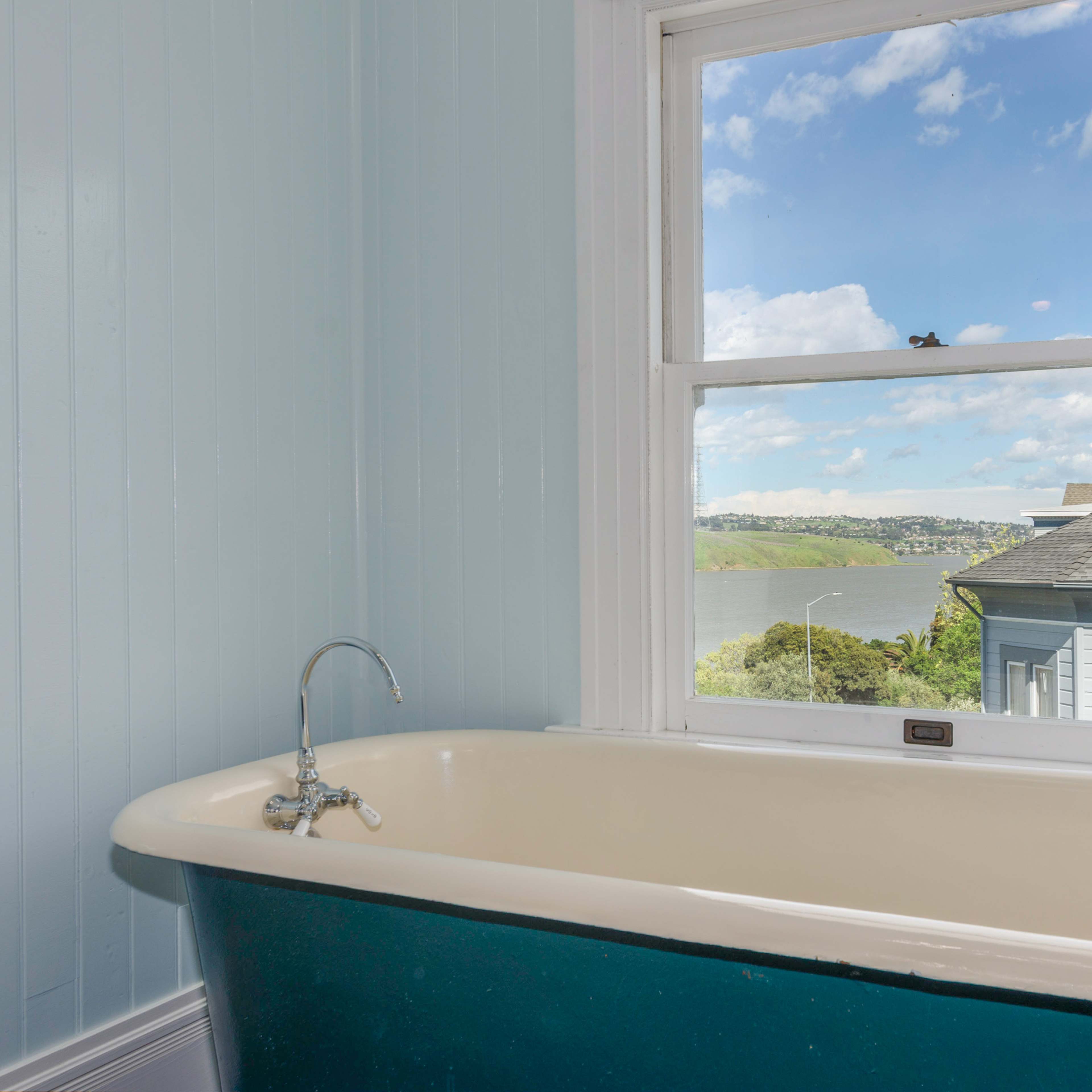 A clawfoot bathtub is positioned near a window that offers a view of a scenic landscape and water.