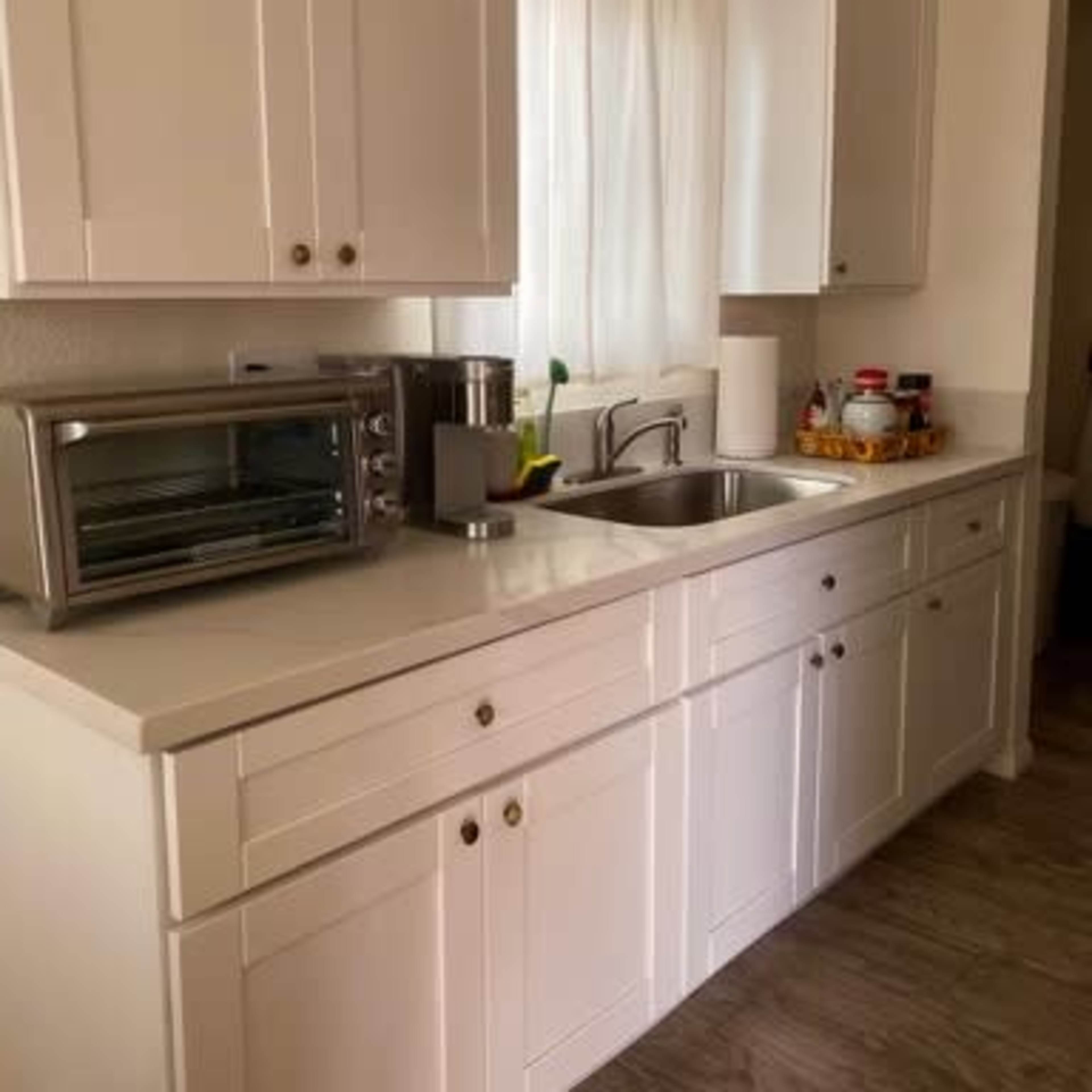 A kitchen with white cabinets, a stainless steel sink, an electric toaster oven, and various condiments on the counter.