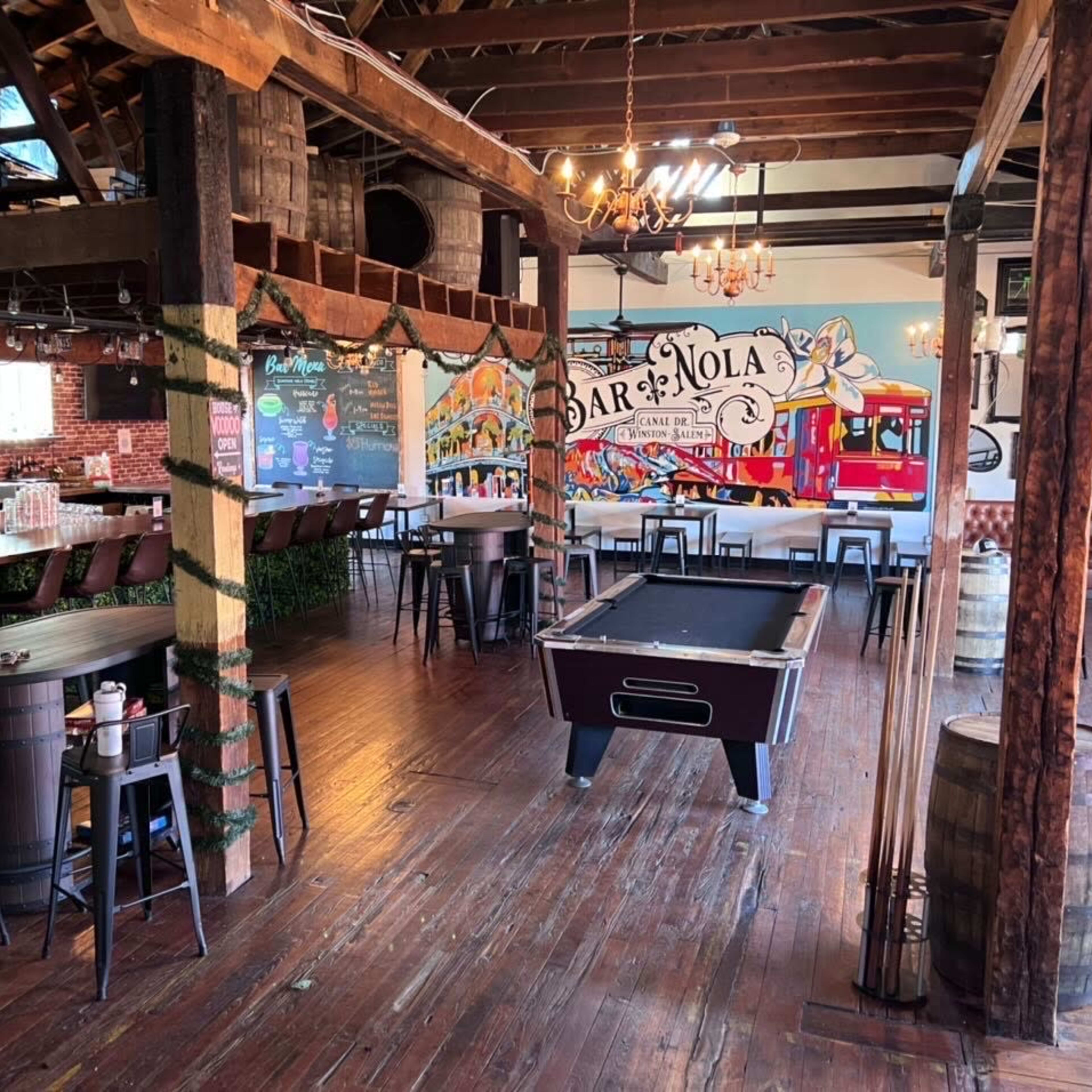 A lively bar interior featuring a pool table, a long wooden bar, and colorful murals on the walls.