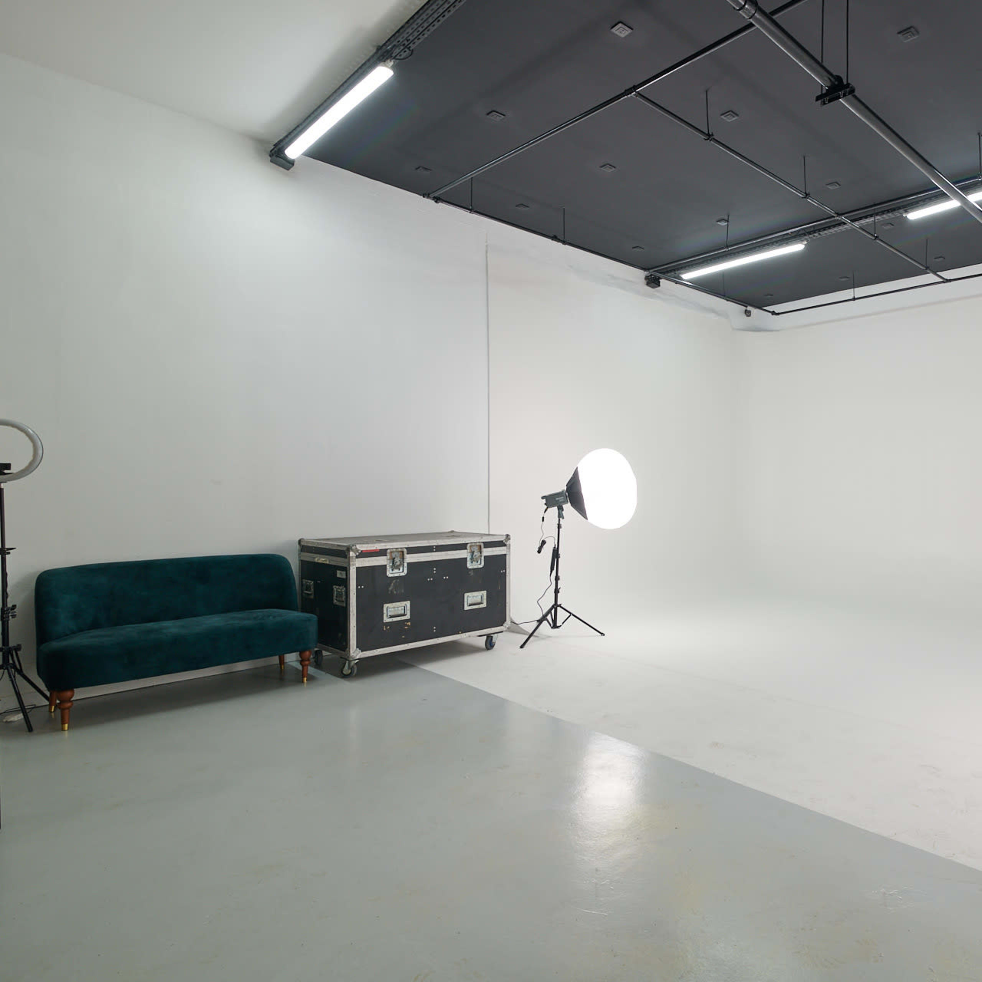 A minimalistic photo studio features a white backdrop, two light setups, and a green velvet sofa on one side.