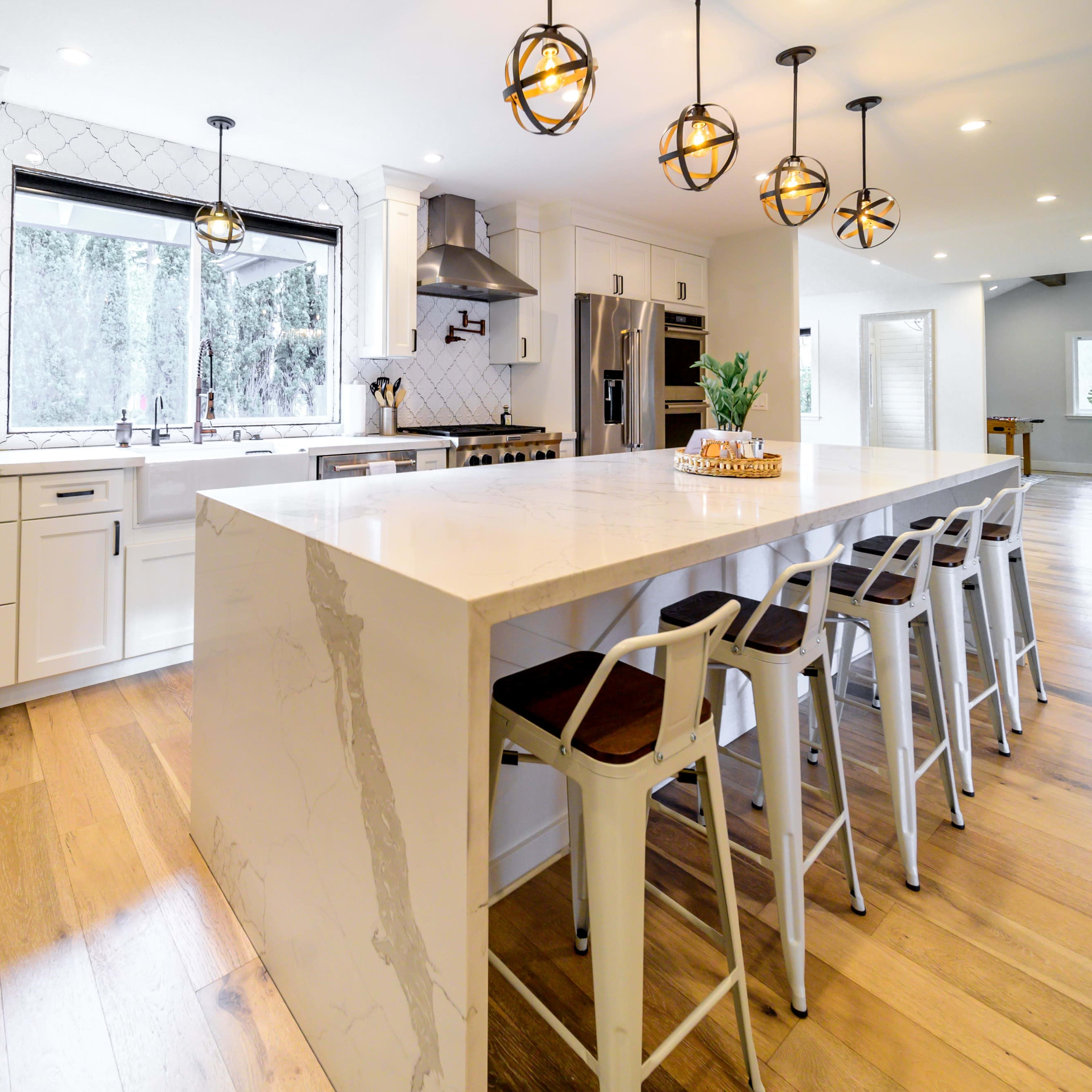 A modern kitchen with a large island, white cabinetry, and pendant lights, featuring barstools alongside the island.