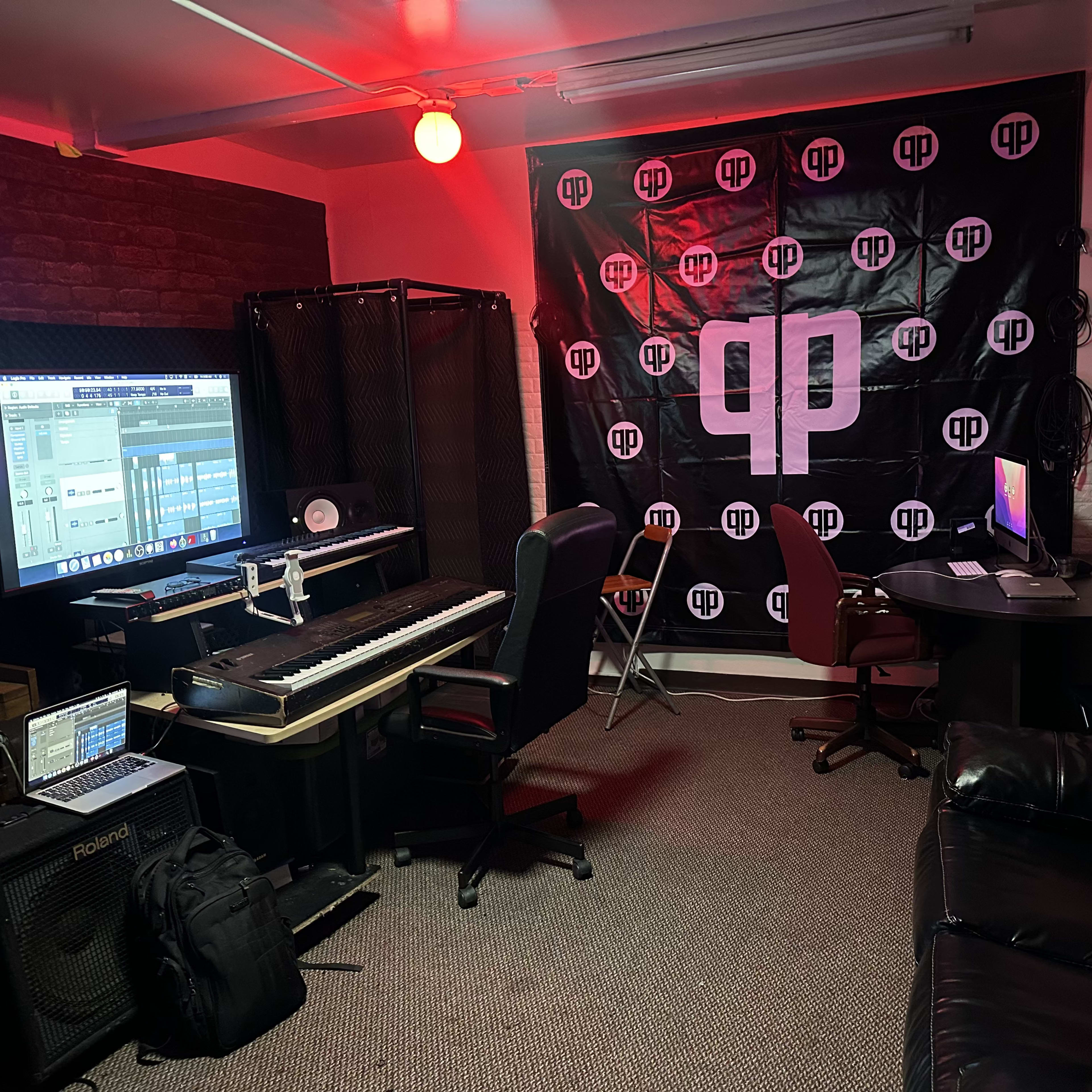 A music production studio with a keyboard, multiple screens, a large banner, and seating areas.