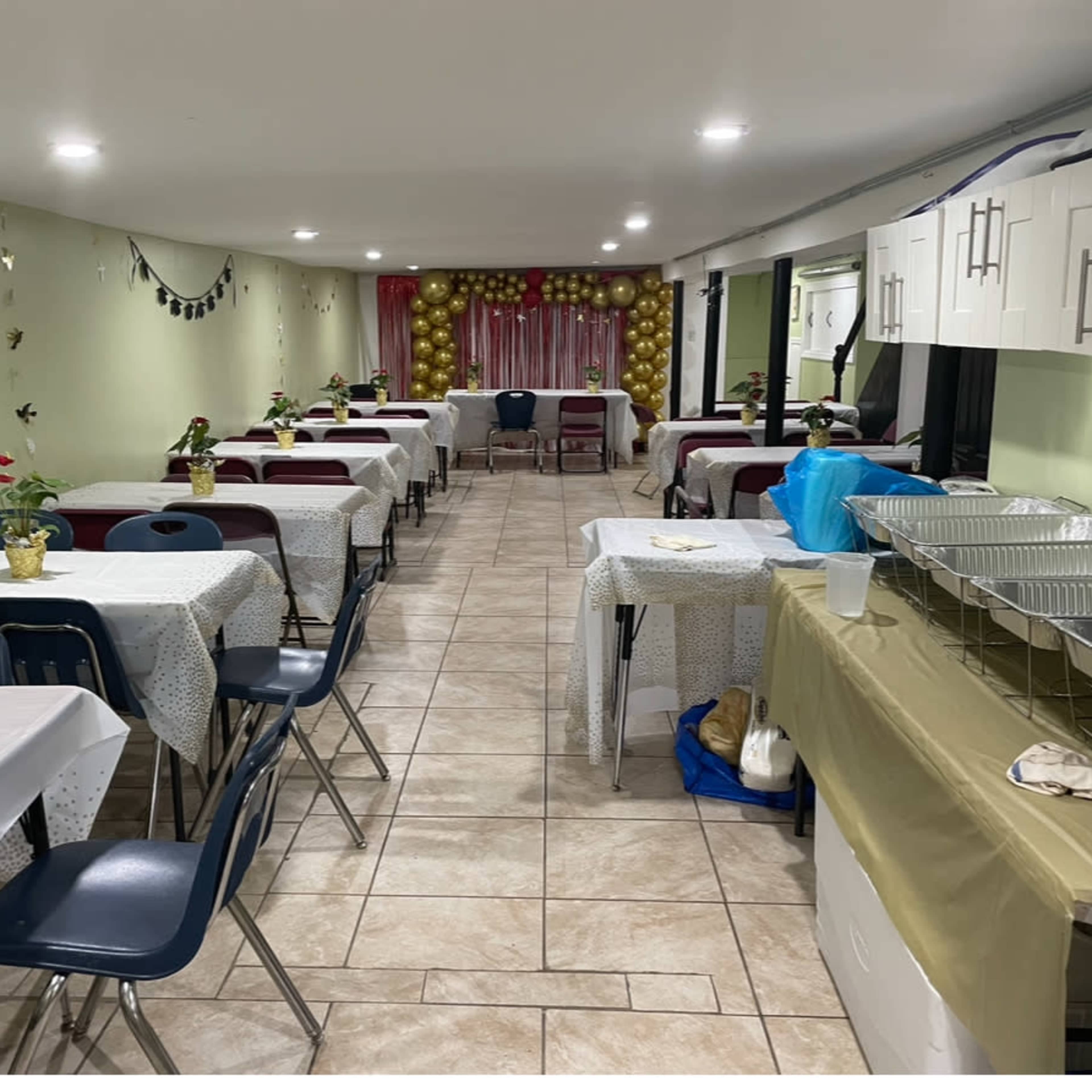 A dining area set with several tables covered in tablecloths, with decorations and a serving area at one end.