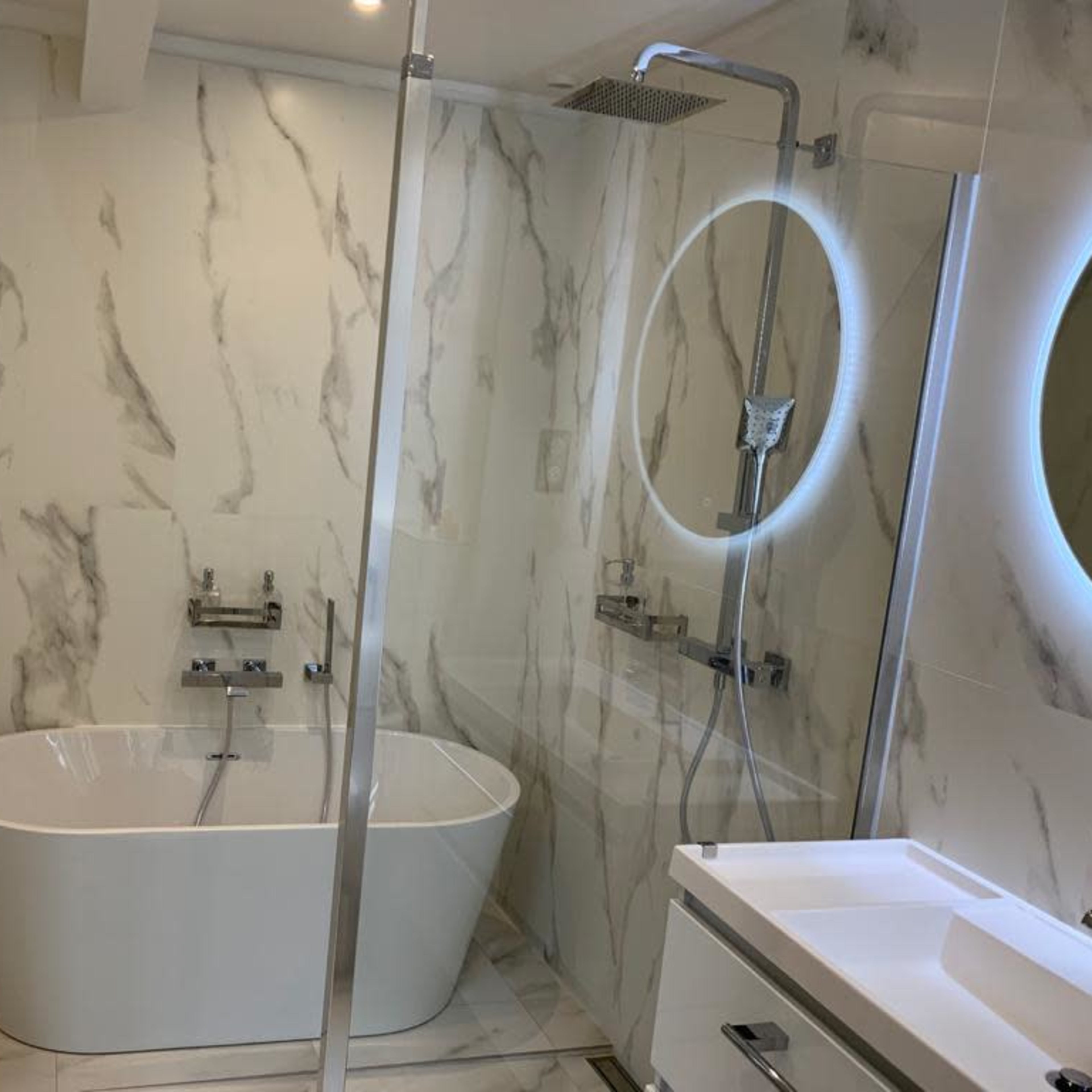 A modern bathroom featuring a freestanding bathtub, a glass shower enclosure, and marble-like wall tiles.