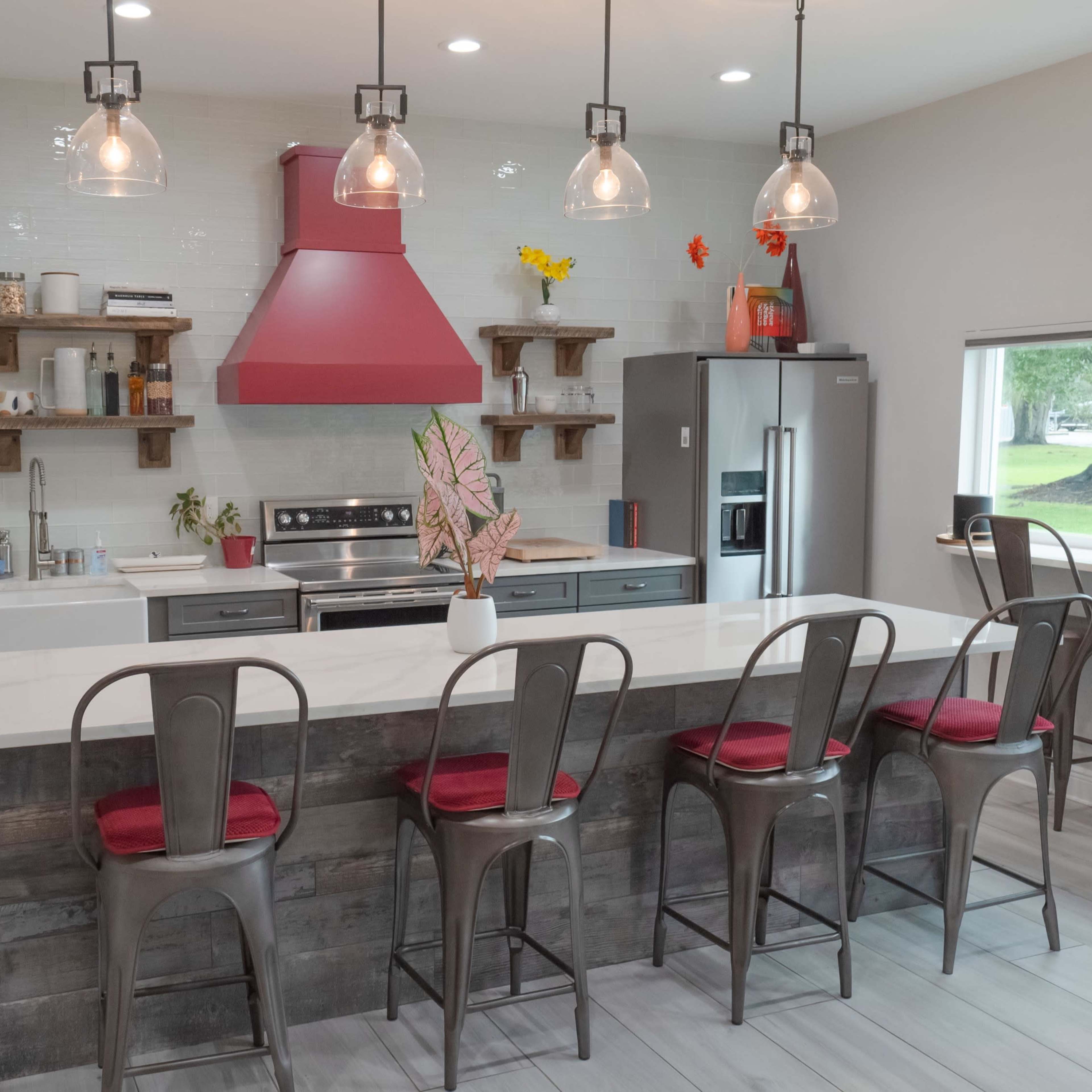 A modern kitchen features a central island with bar seating, stainless steel appliances, and a red range hood above the stove.