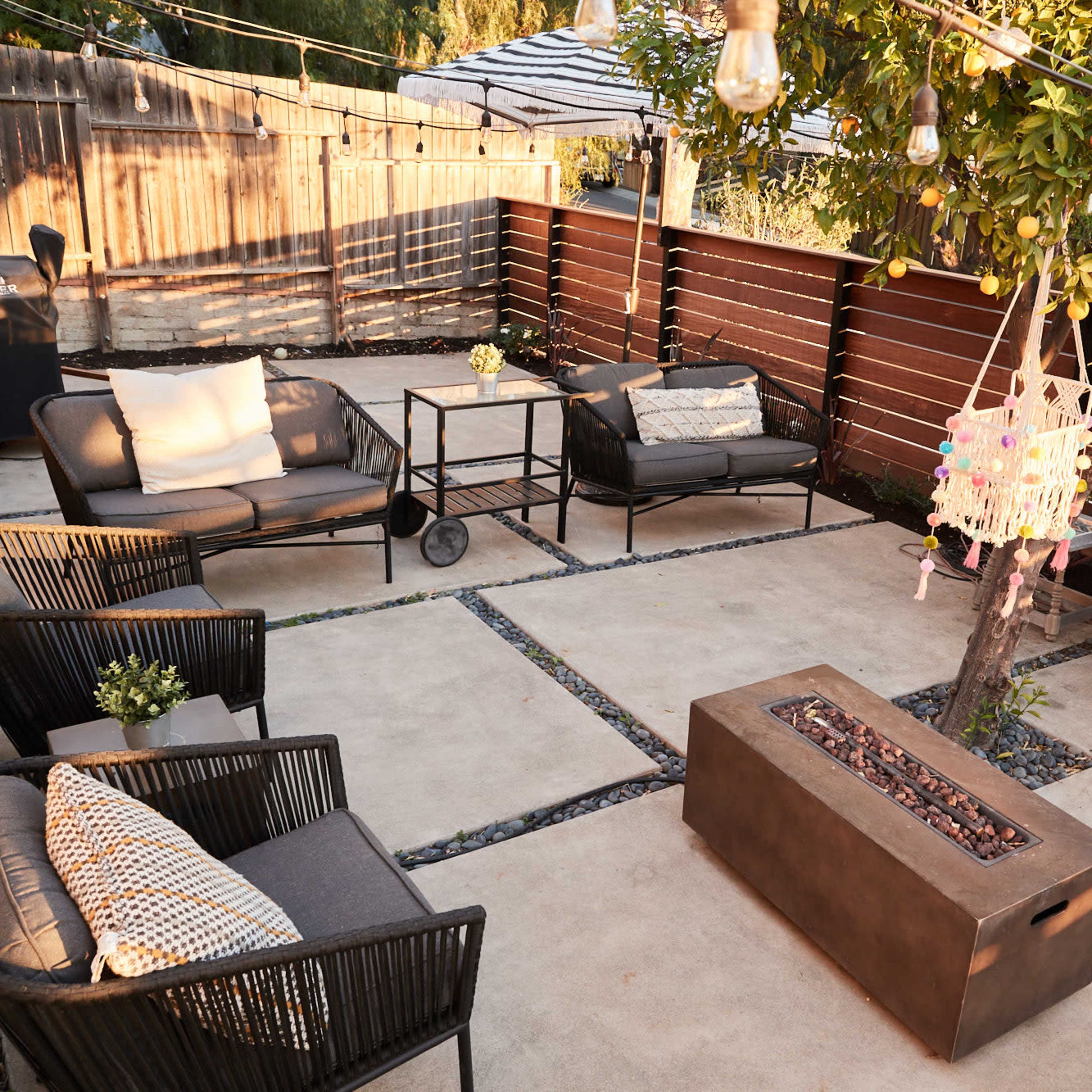 A well-arranged outdoor patio with seating areas, a fire pit, and decorative lighting, surrounded by wooden fencing and greenery.