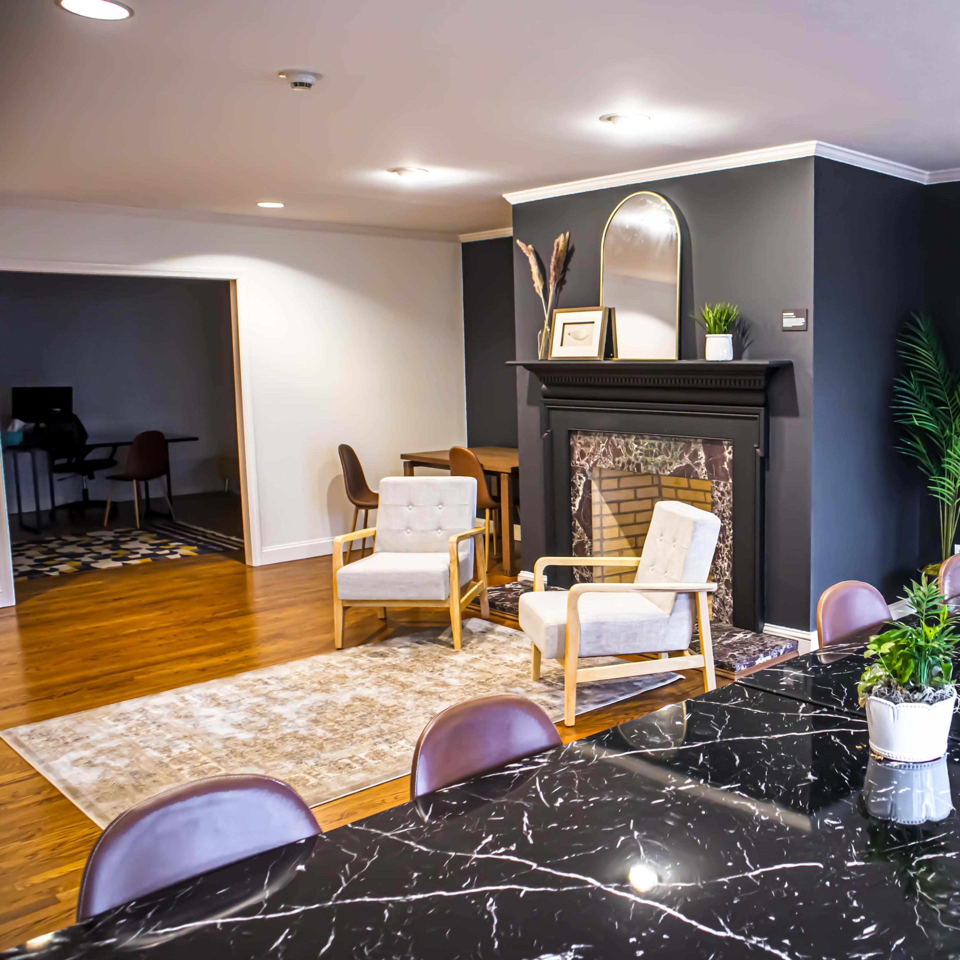 A modern interior space featuring a dining area with a black marble table, brown chairs, and a cozy seating arrangement by a fireplace.