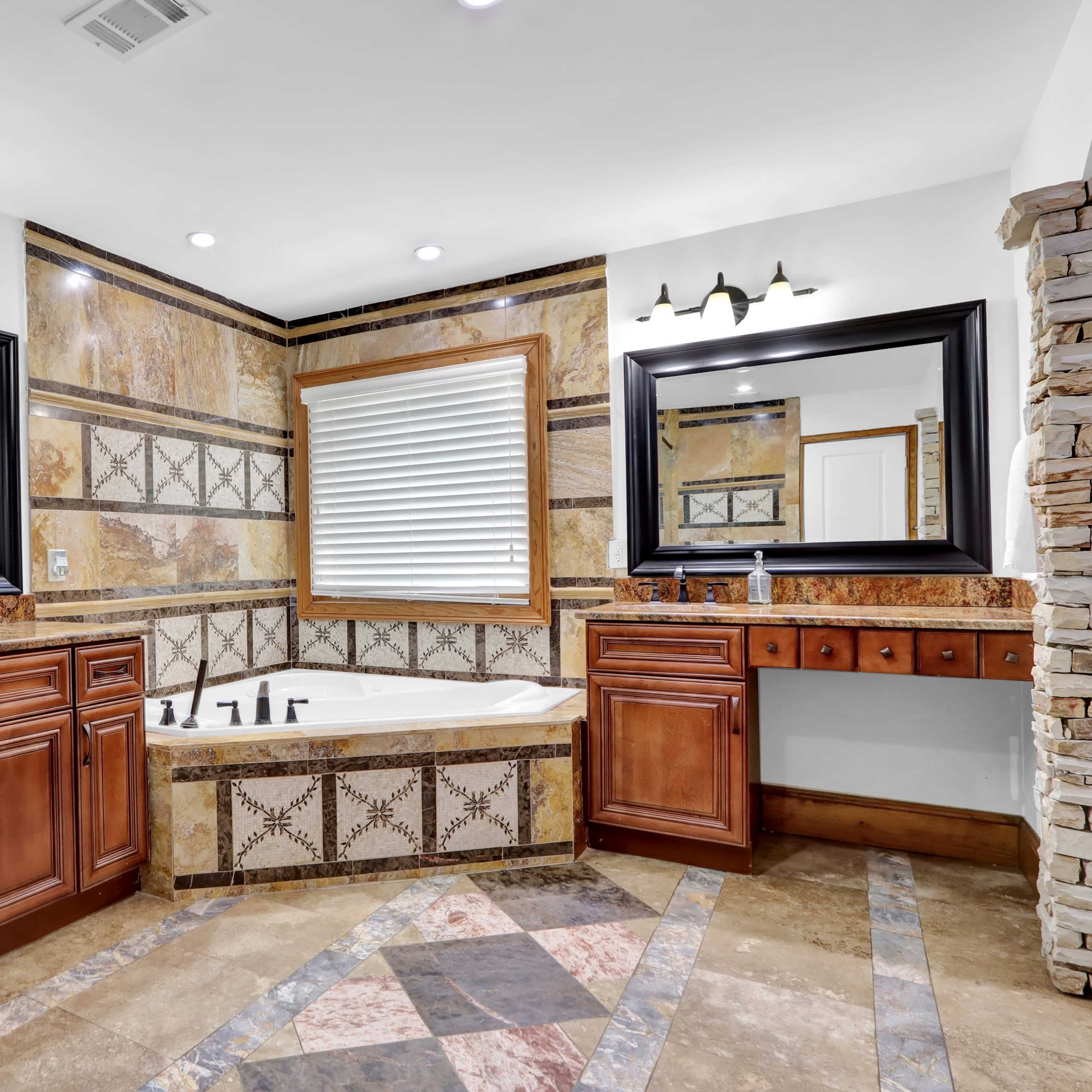 A modern bathroom featuring a jetted bathtub surrounded by marble finishes, wooden cabinetry, and two large mirrors.