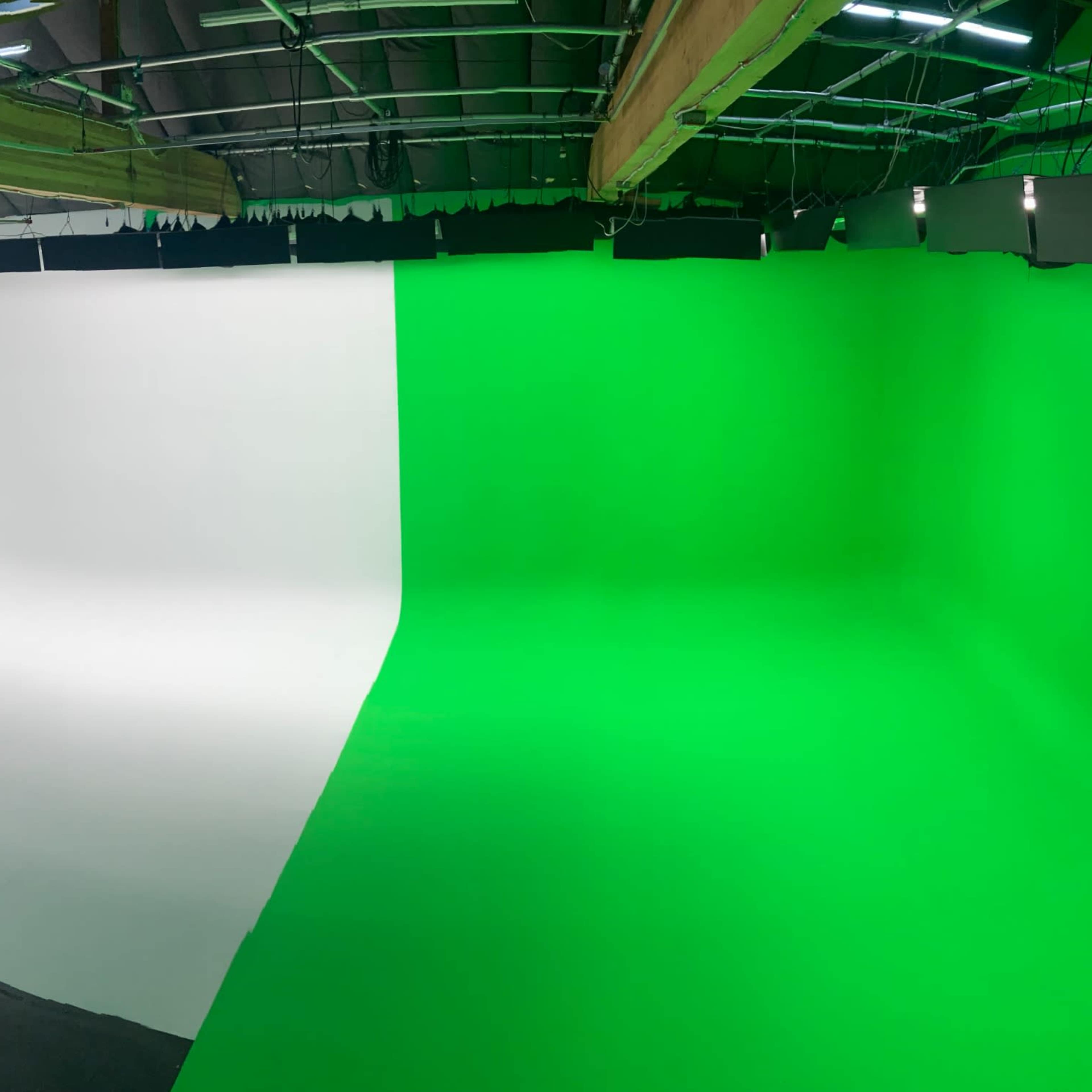 A panoramic view of a photography studio featuring a white backdrop on one side and a green screen backdrop on the other.