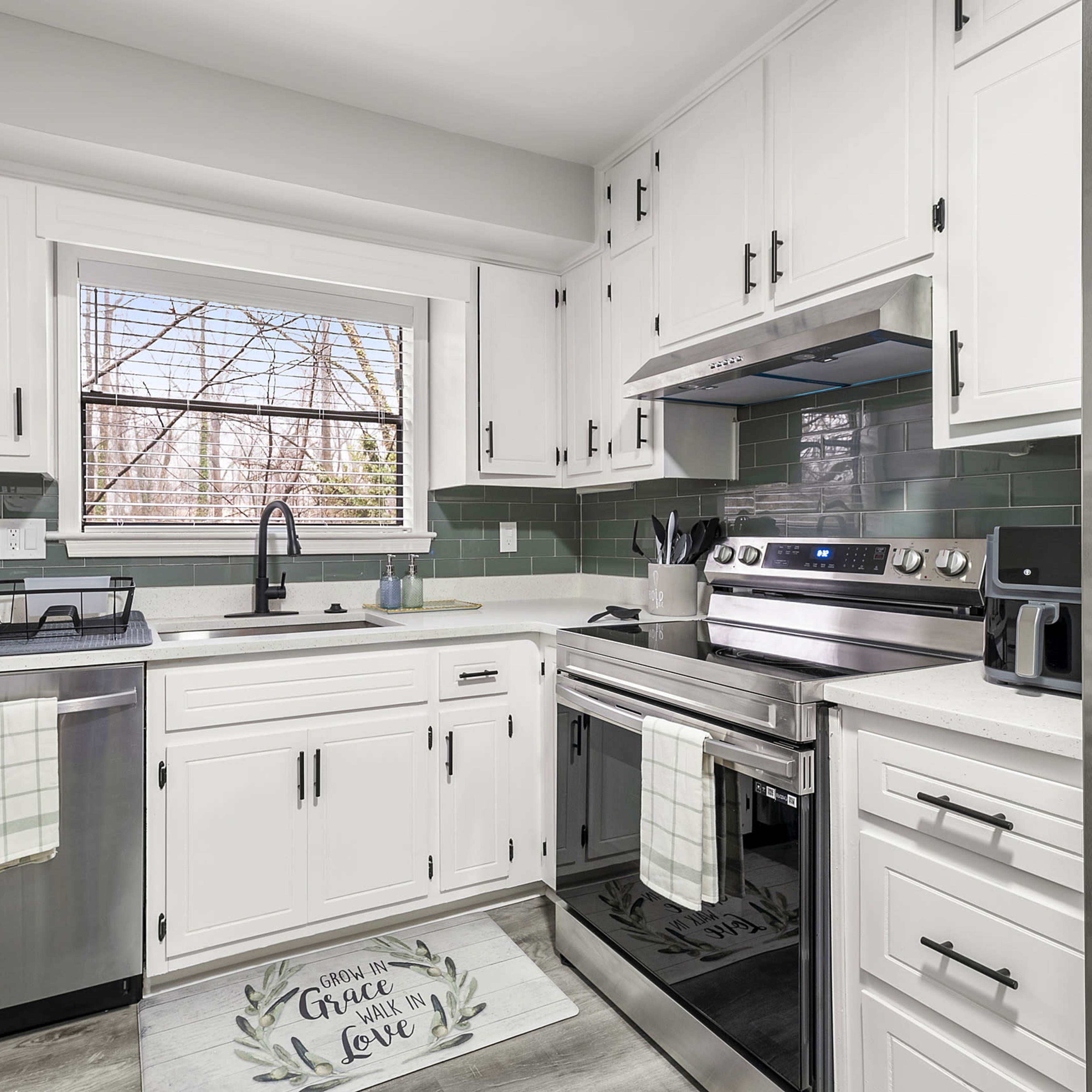 A modern kitchen with white cabinets, stainless steel appliances, and green tiled backsplash.