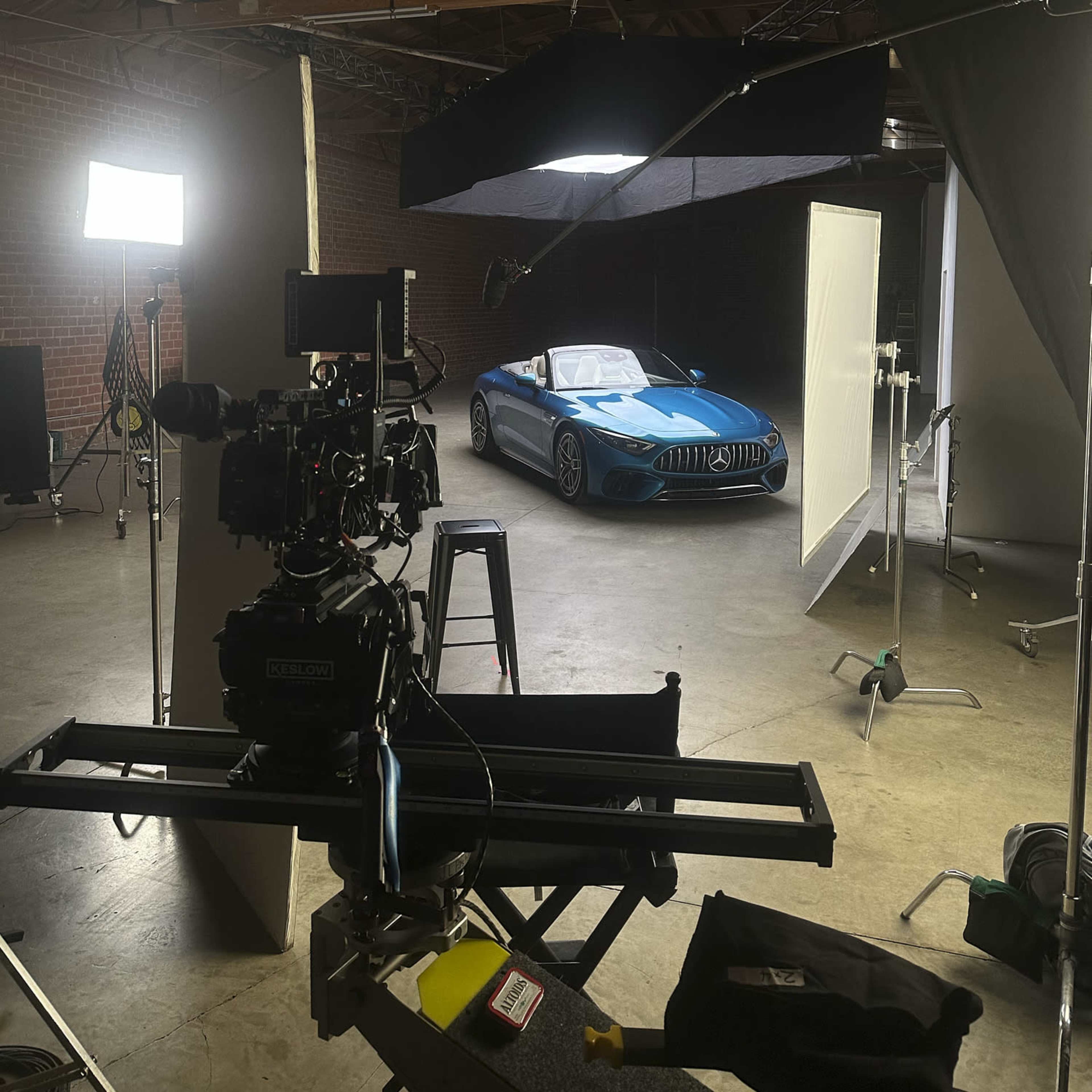 A camera setup is positioned in a studio, focusing on a blue sports car parked under studio lights.