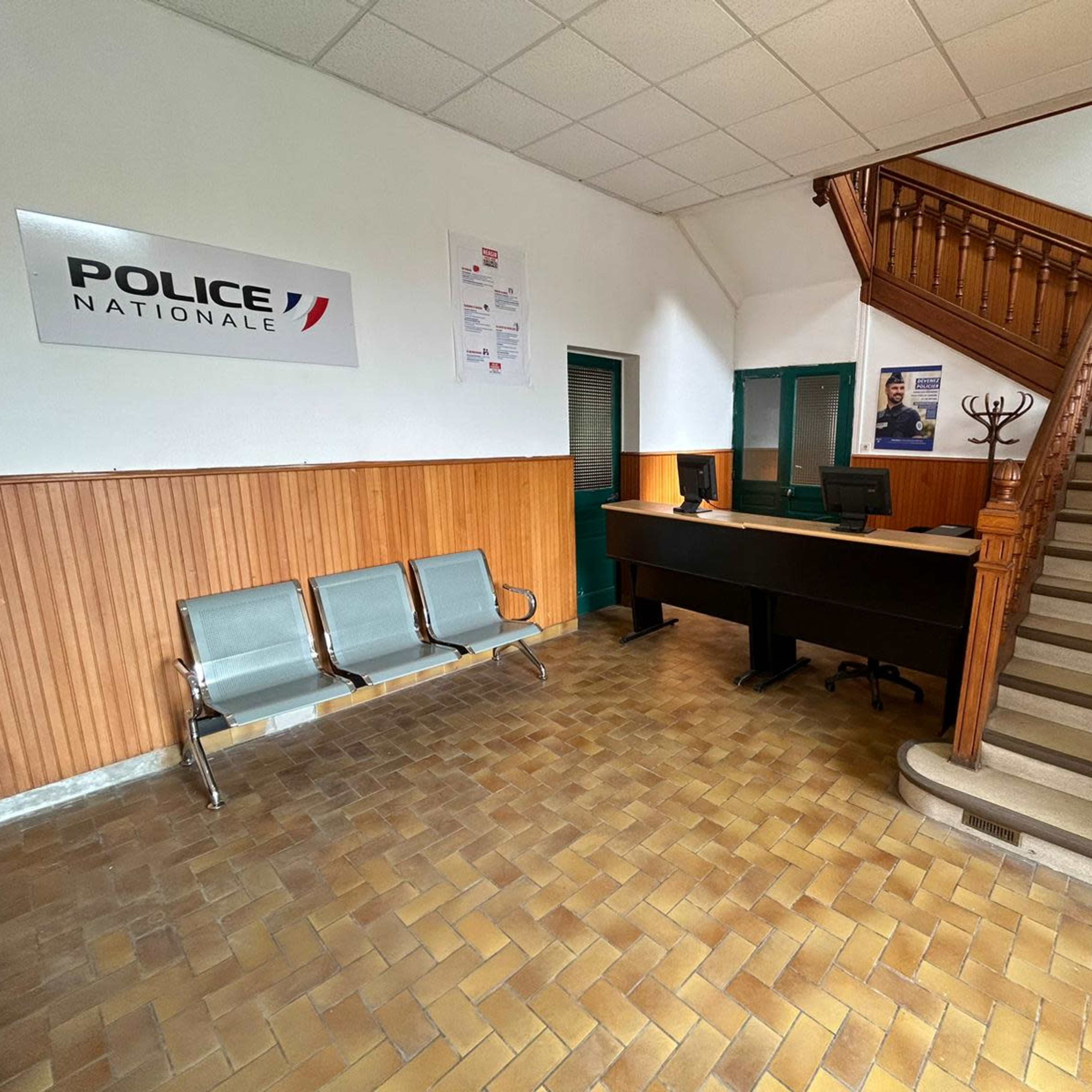 A police station interior with a reception desk, seating area, and a staircase.