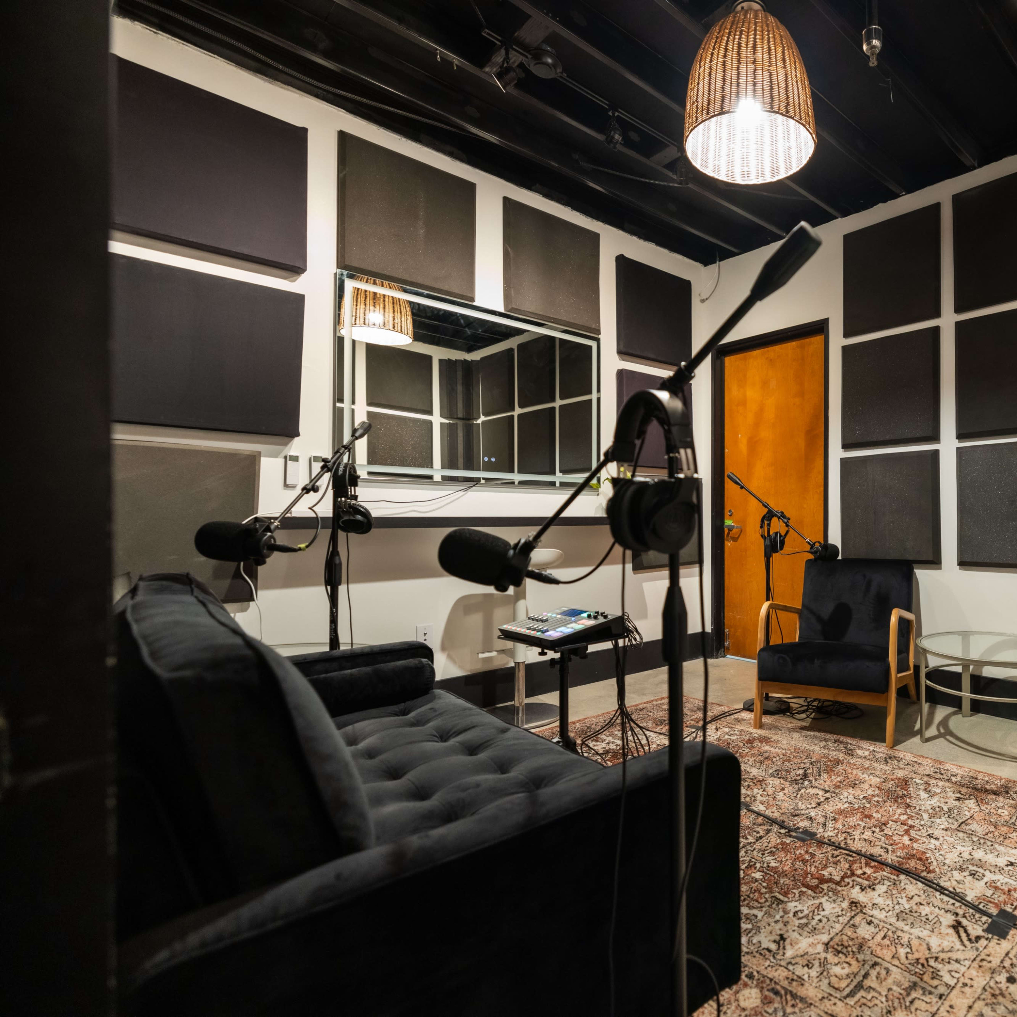A small recording studio with soundproofed walls, two chairs, a table, and several microphones positioned around the room.