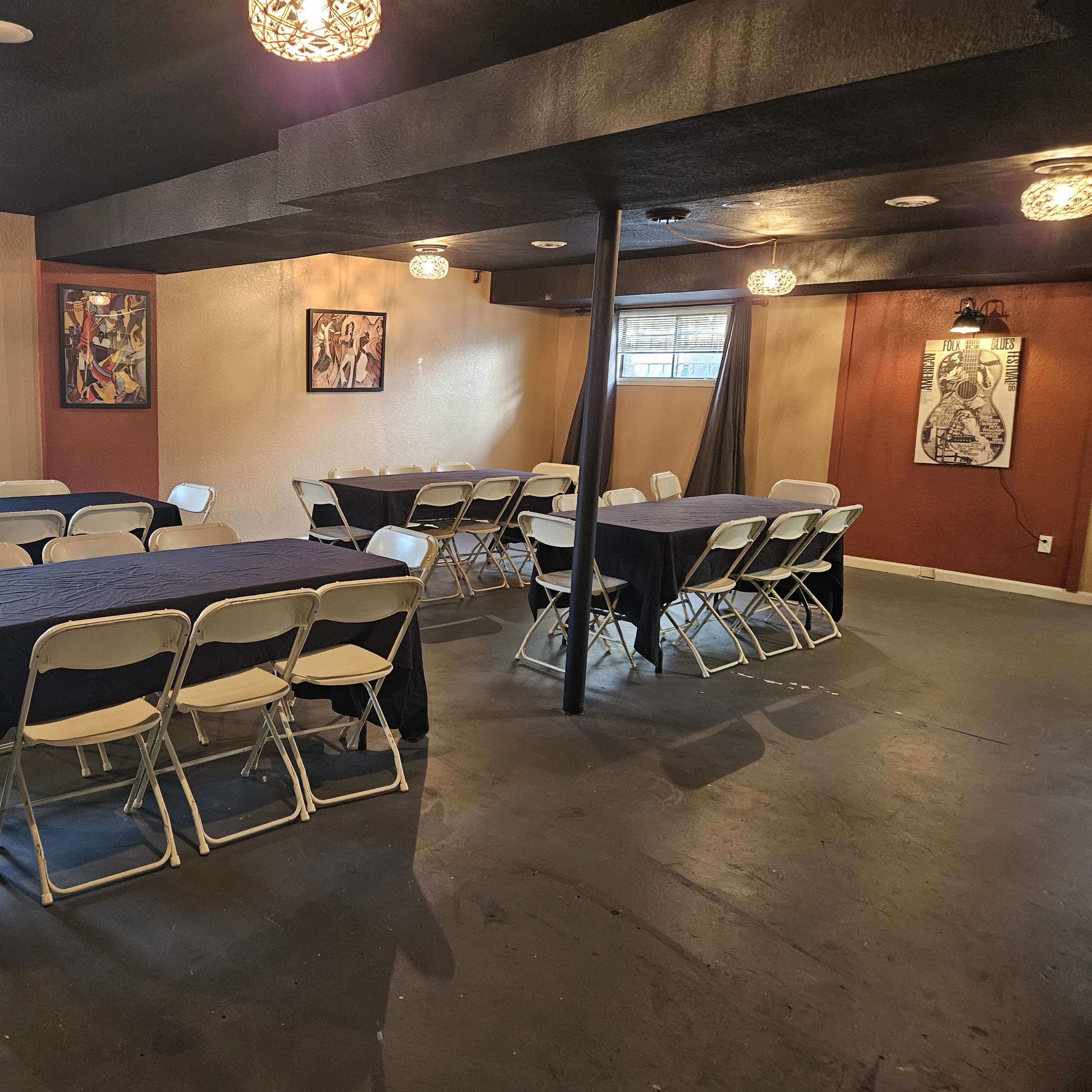 A room with multiple tables covered in black cloth, surrounded by chairs, and decorated with wall art and pendant lights.