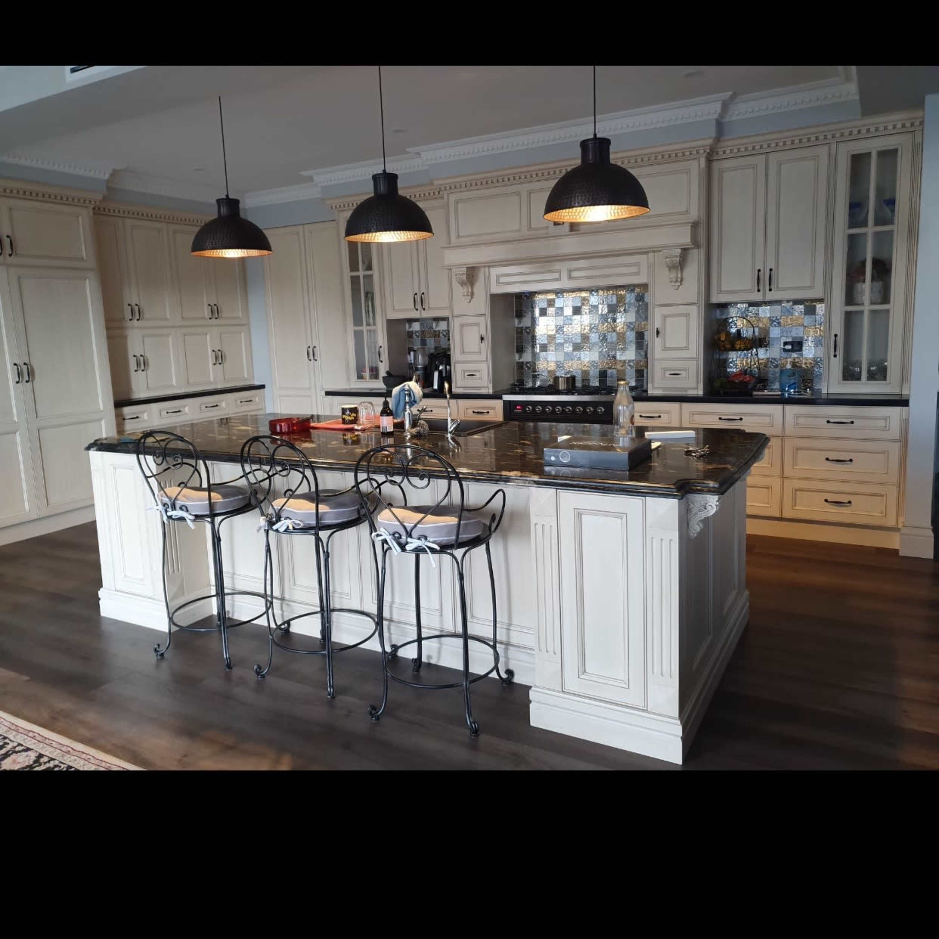 A kitchen with a central island featuring bar stools and pendant lights, wooden flooring, and cabinetry in a light color.