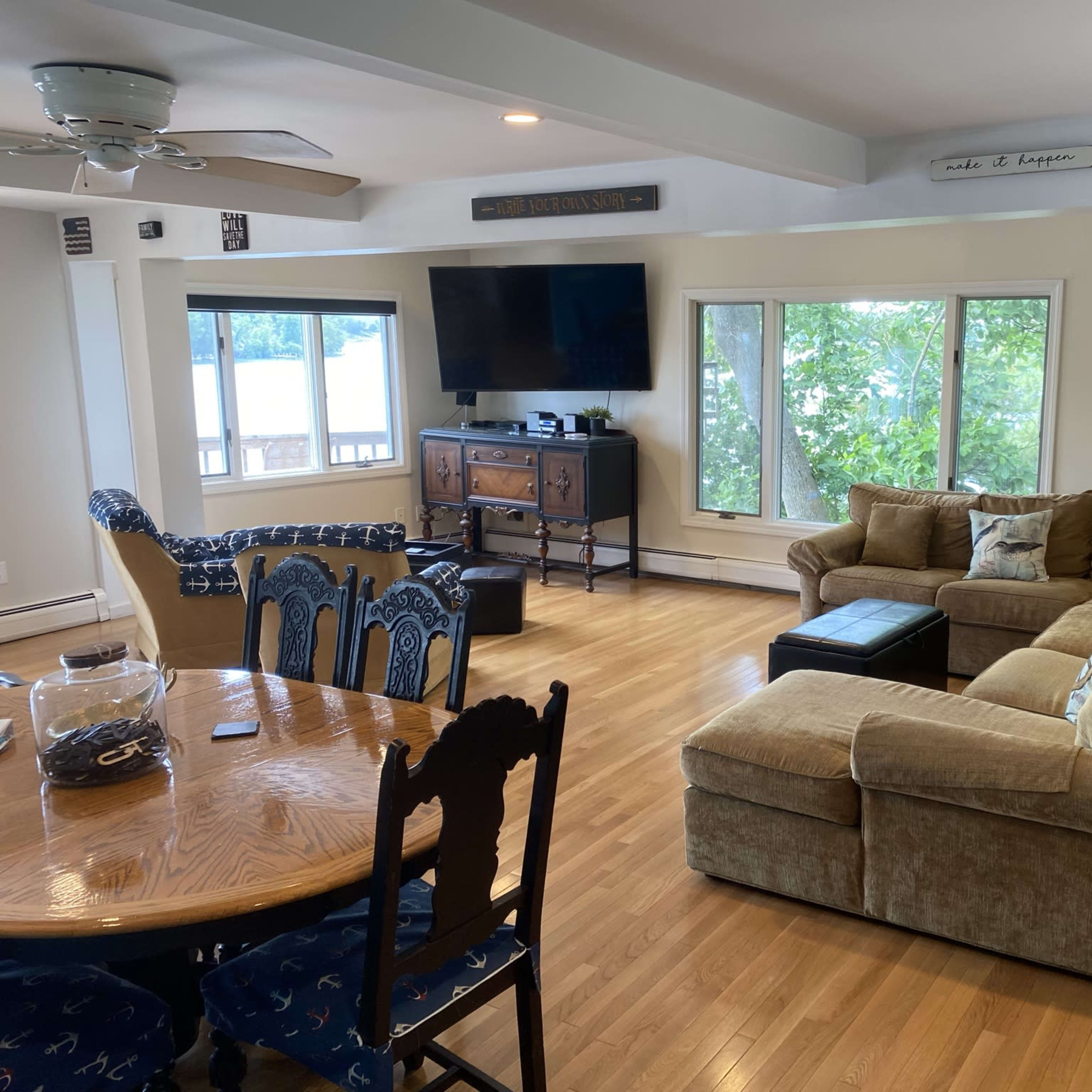 A spacious living area featuring a sectional sofa, a coffee table, a television, and large windows overlooking a body of water.