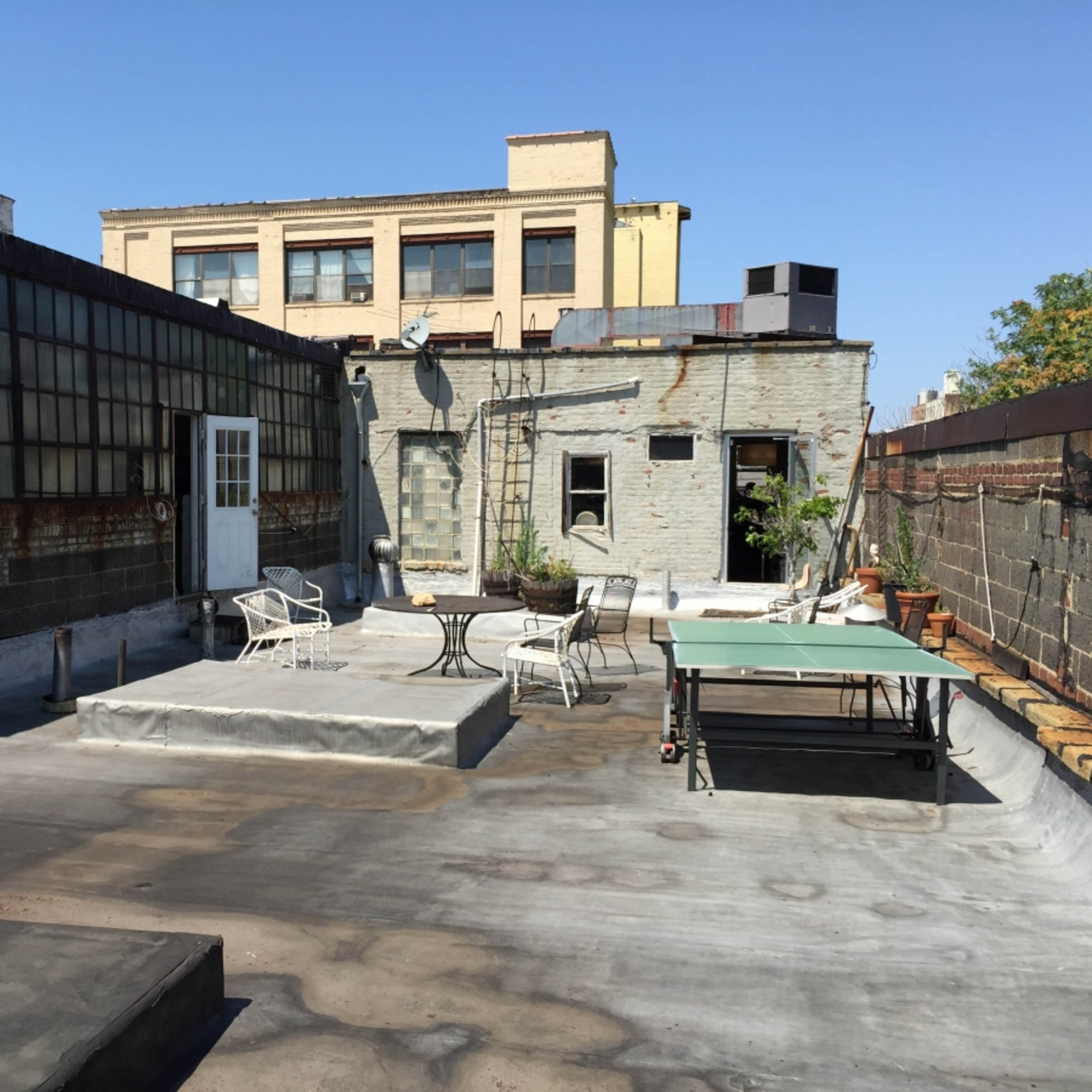 A rooftop space with a few chairs, a table, and a ping pong table, surrounded by walls and a clear blue sky.