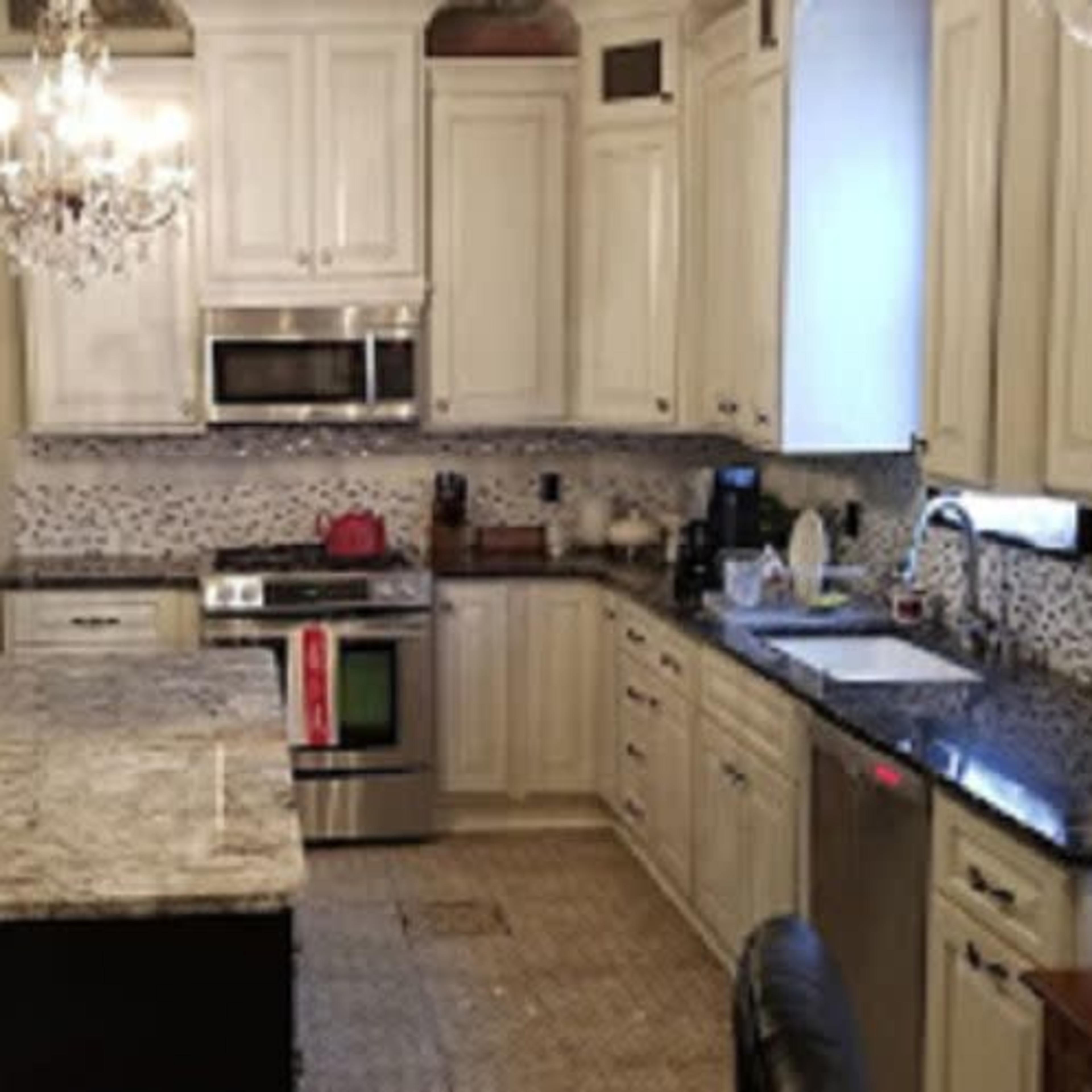 A modern kitchen with white cabinetry, a central island with a granite countertop, stainless steel appliances, and decorative chandeliers overhead.