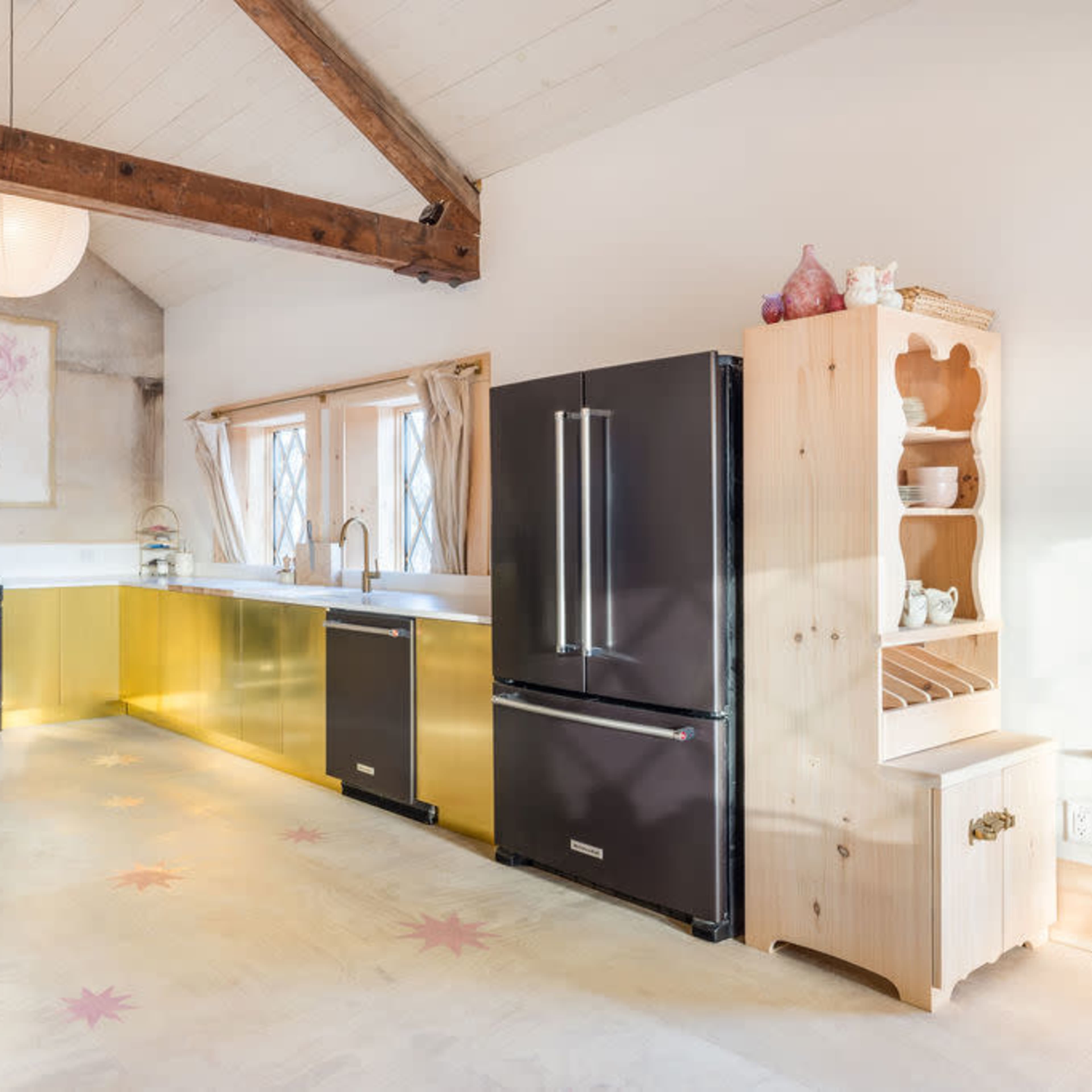A modern kitchen features golden cabinetry, black appliances, and wooden accents under a high ceiling with exposed beams.