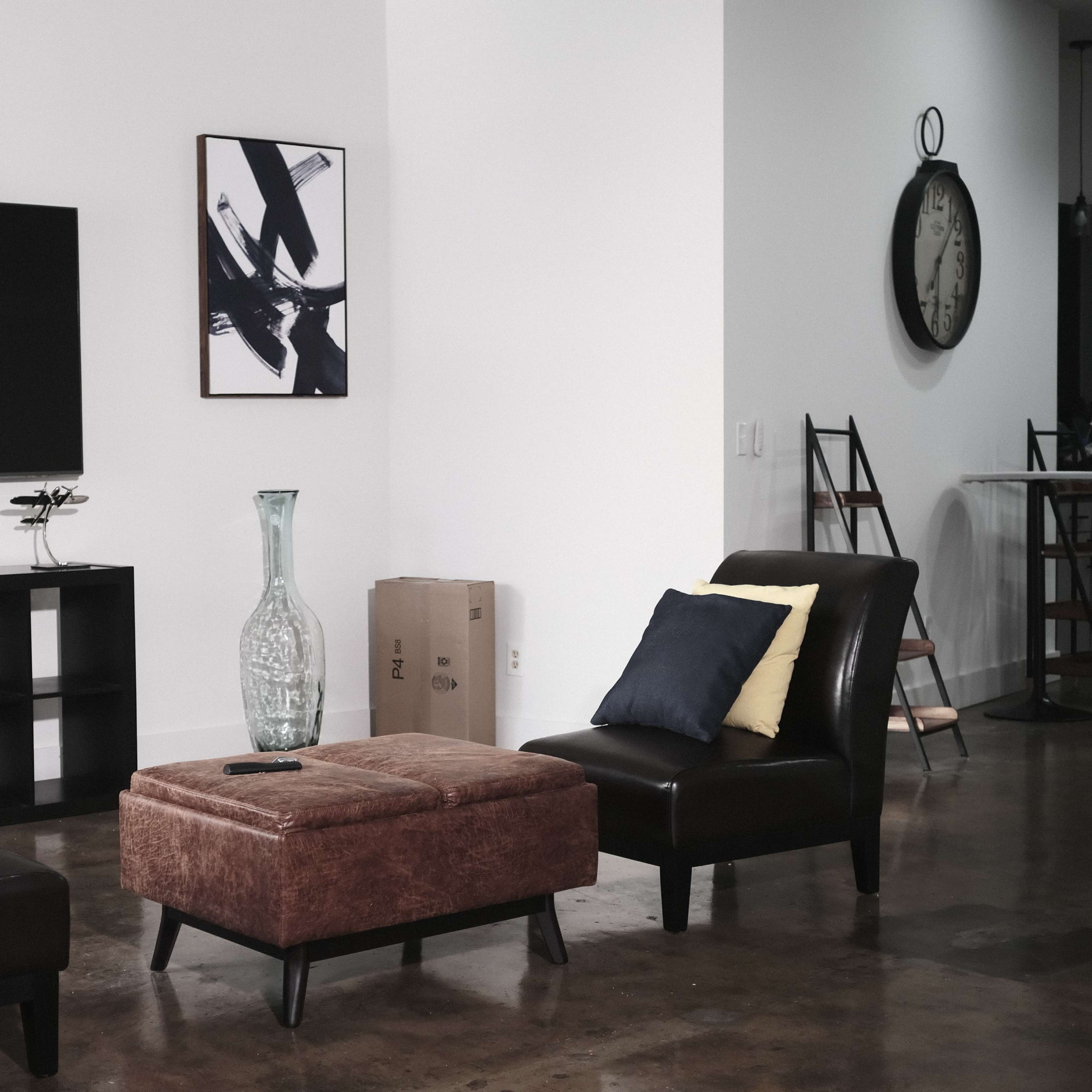 A modern living room features a television on the wall, two chairs with pillows, a glass vase, and a coffee table.