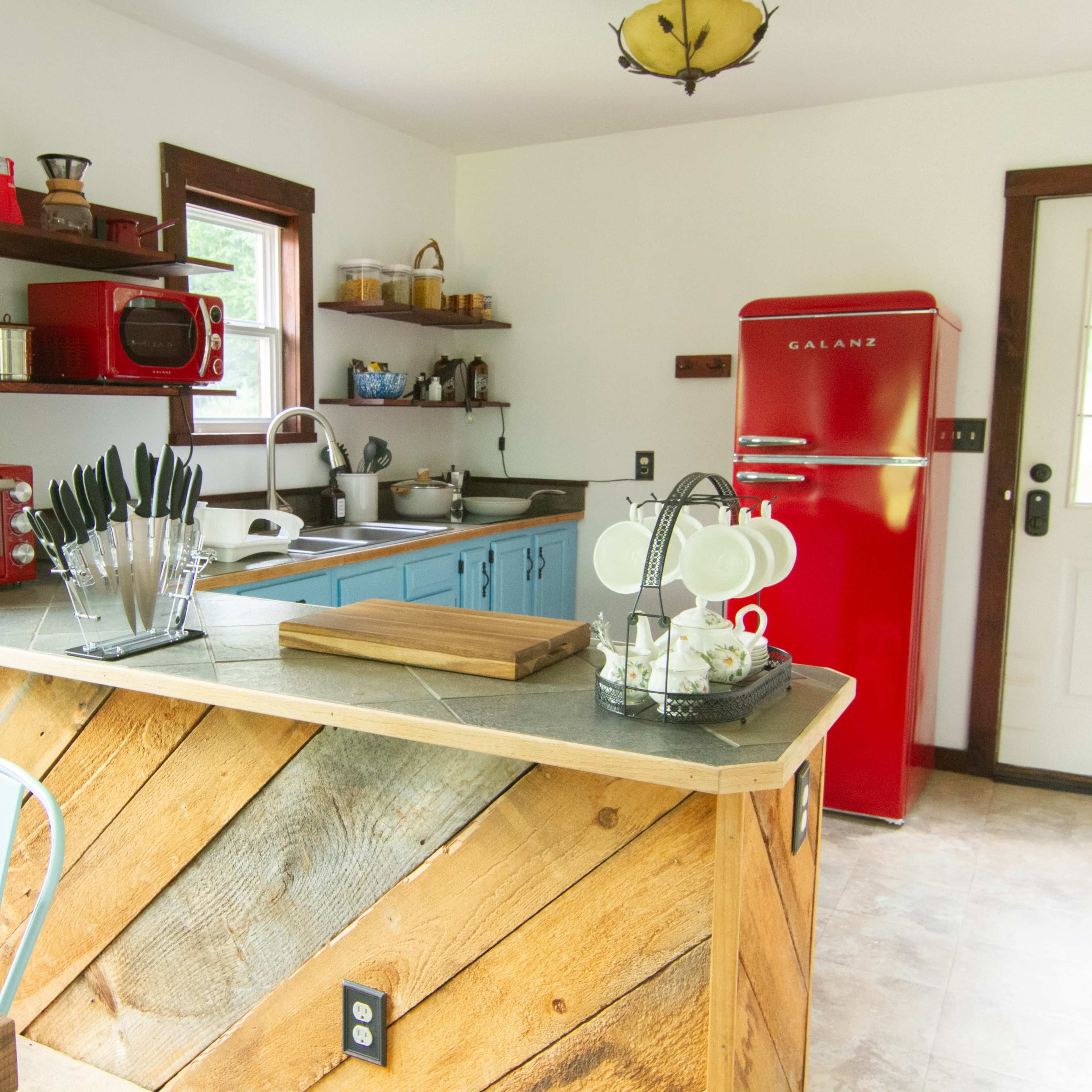A bright kitchen with wooden countertops, blue cabinets, a red refrigerator, and a variety of kitchen appliances and utensils on display.