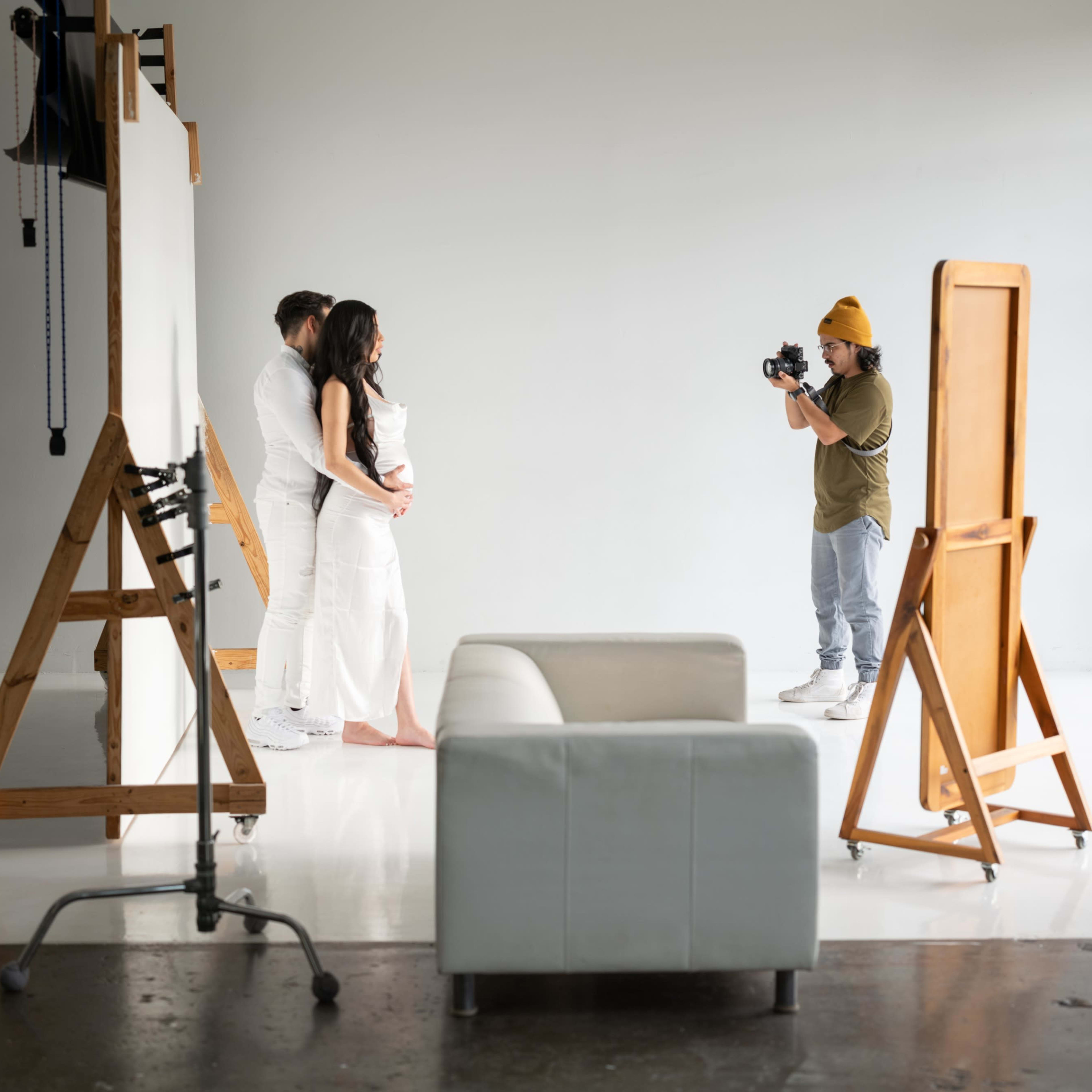 A photographer captures a couple posing in a well-lit studio with large mirrors and a white backdrop.