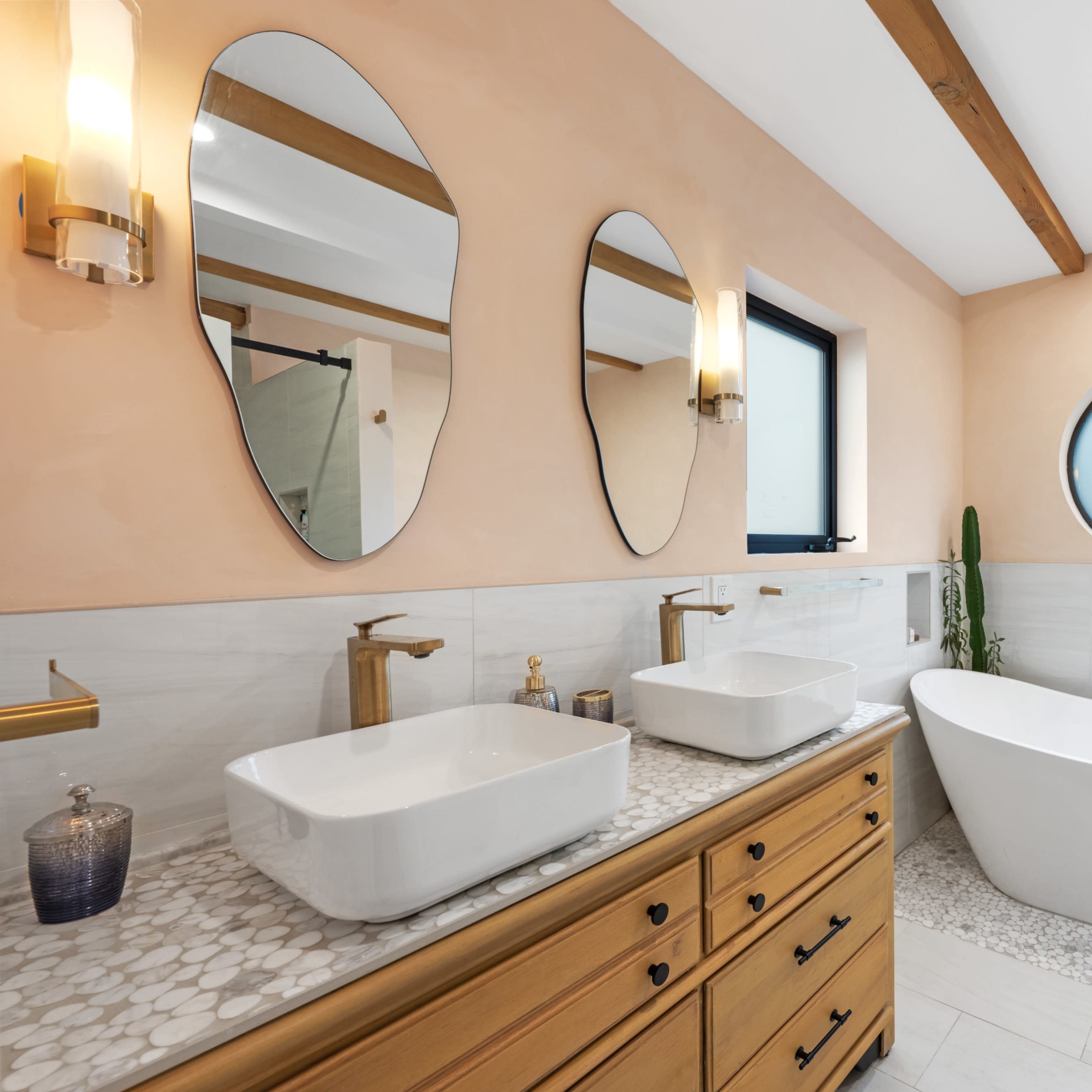 A modern bathroom featuring a freestanding bathtub, double vessel sinks, and three distinct mirrors above a wooden vanity.