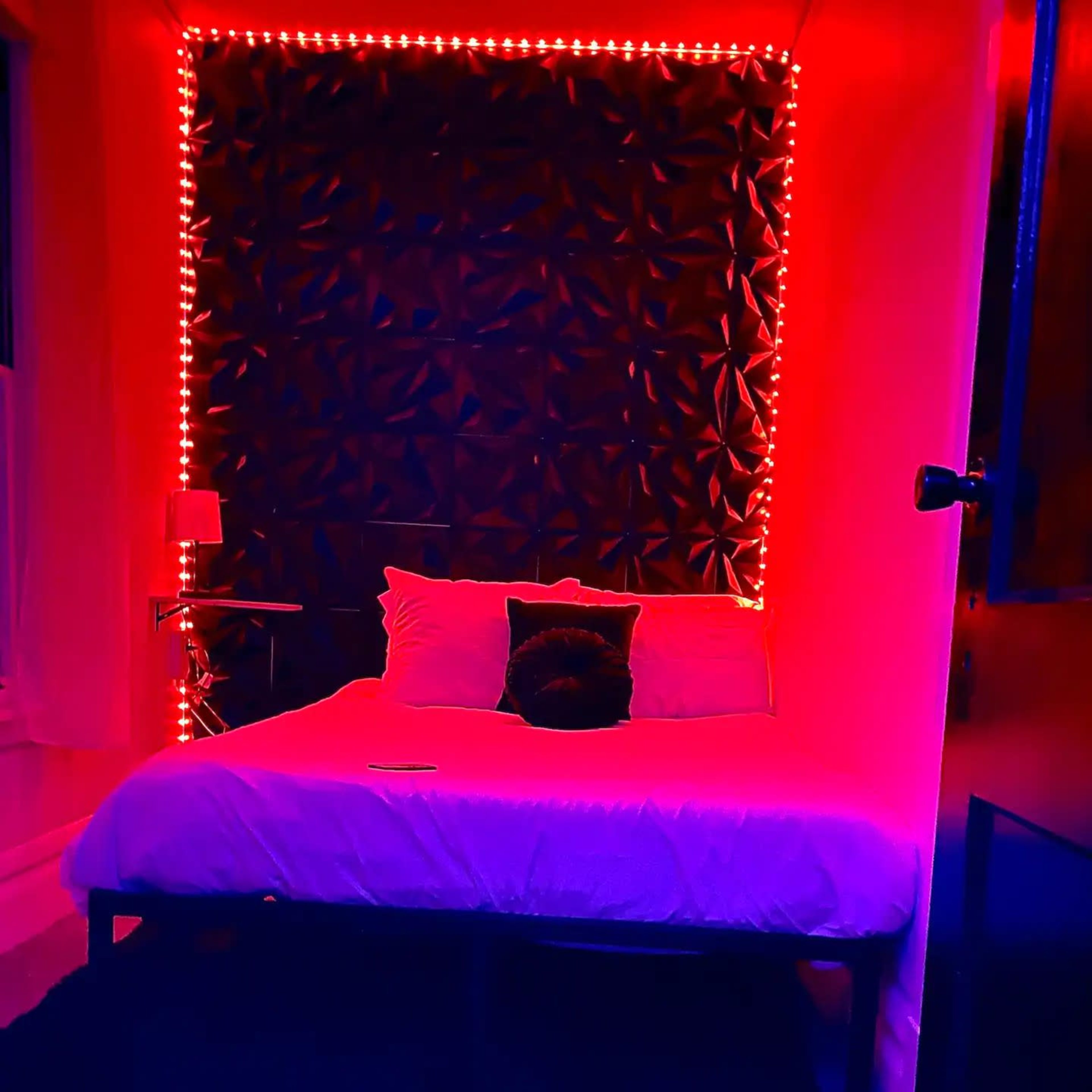 A bedroom with a bed, accented by red LED lights around the wall.