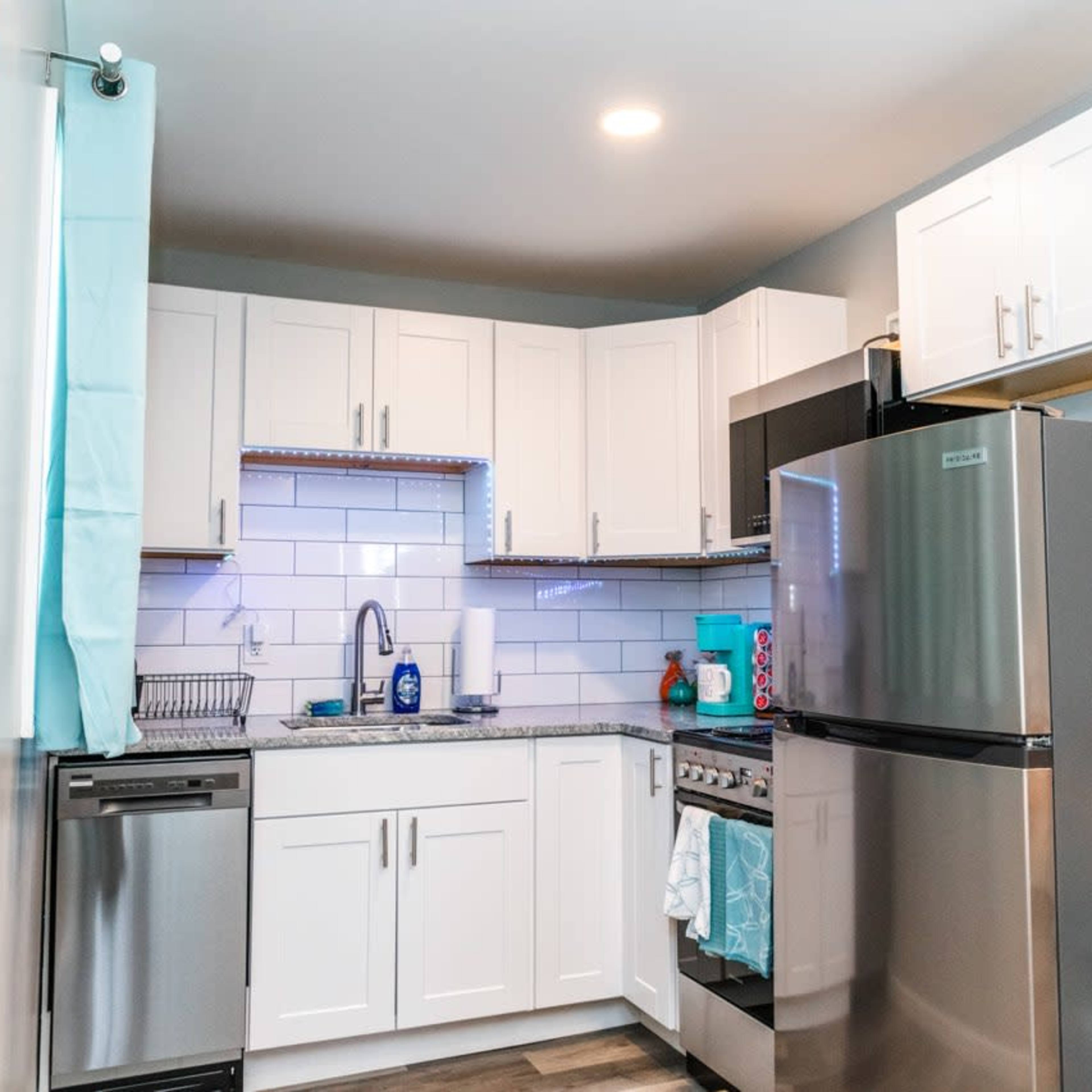 A compact kitchen features white cabinets, stainless steel appliances, and a granite countertop with a contemporary backsplash.