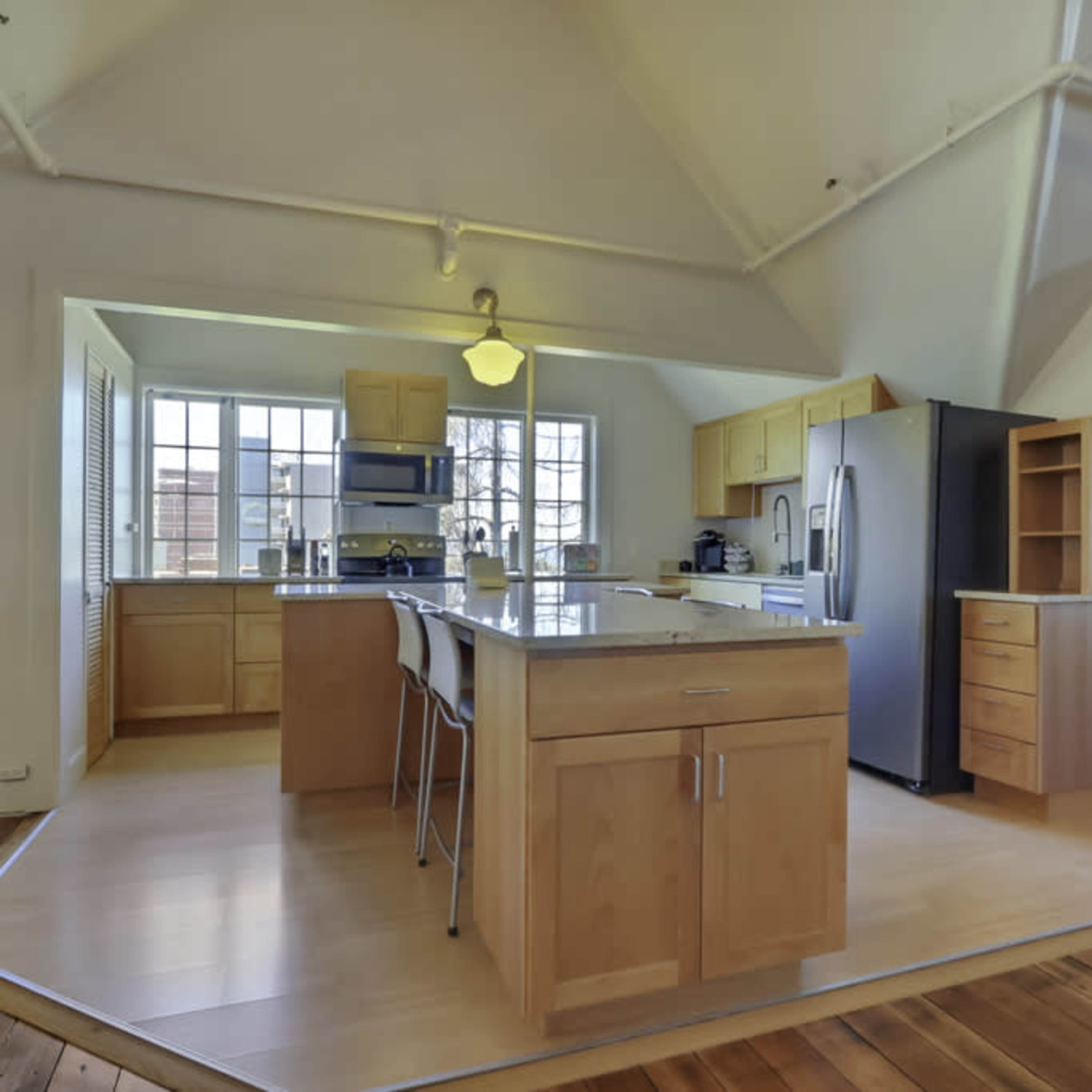 A modern kitchen with wooden cabinets, a central island with seating, and stainless steel appliances.