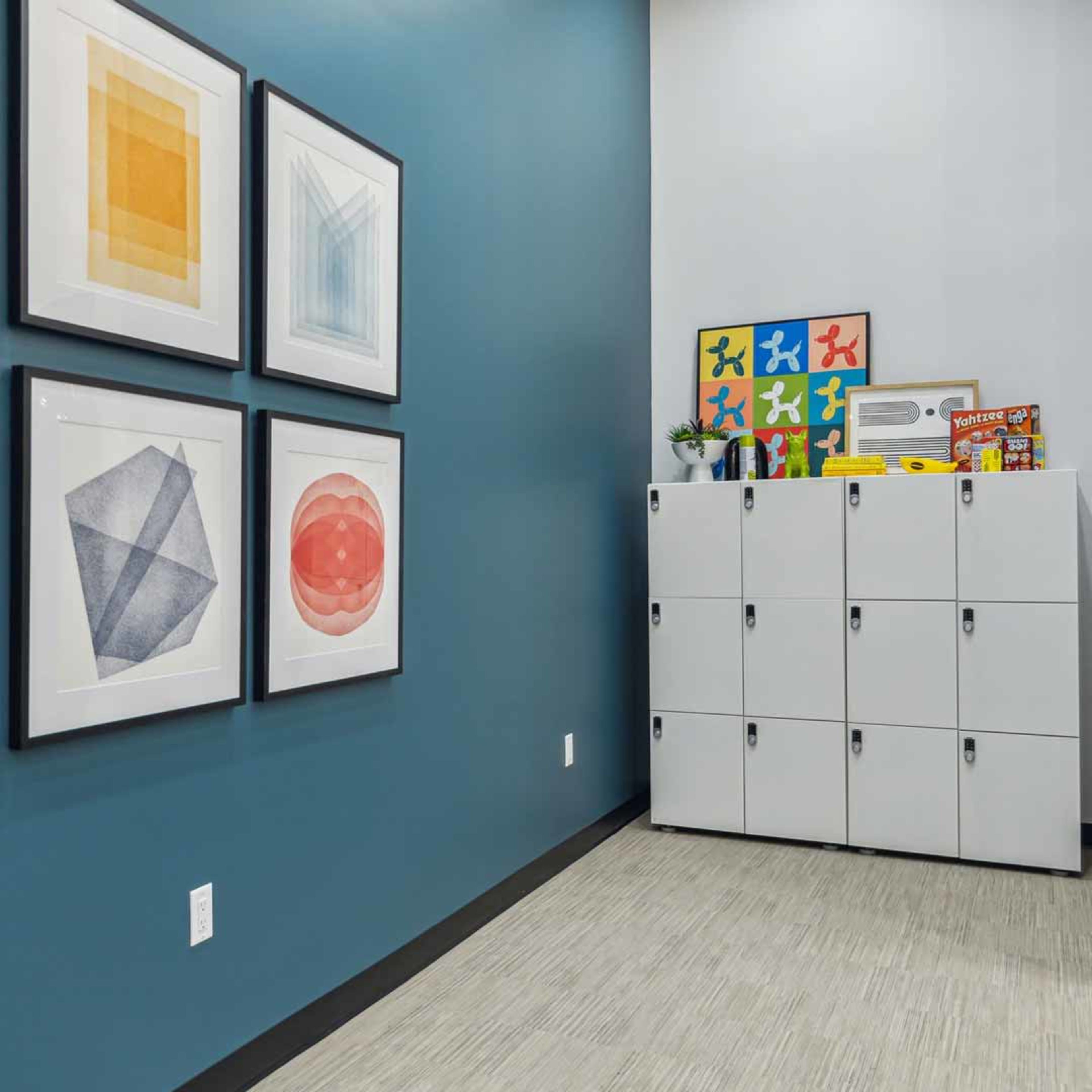 A corner of a room with framed geometric art hanging on a blue wall next to a row of white lockers.