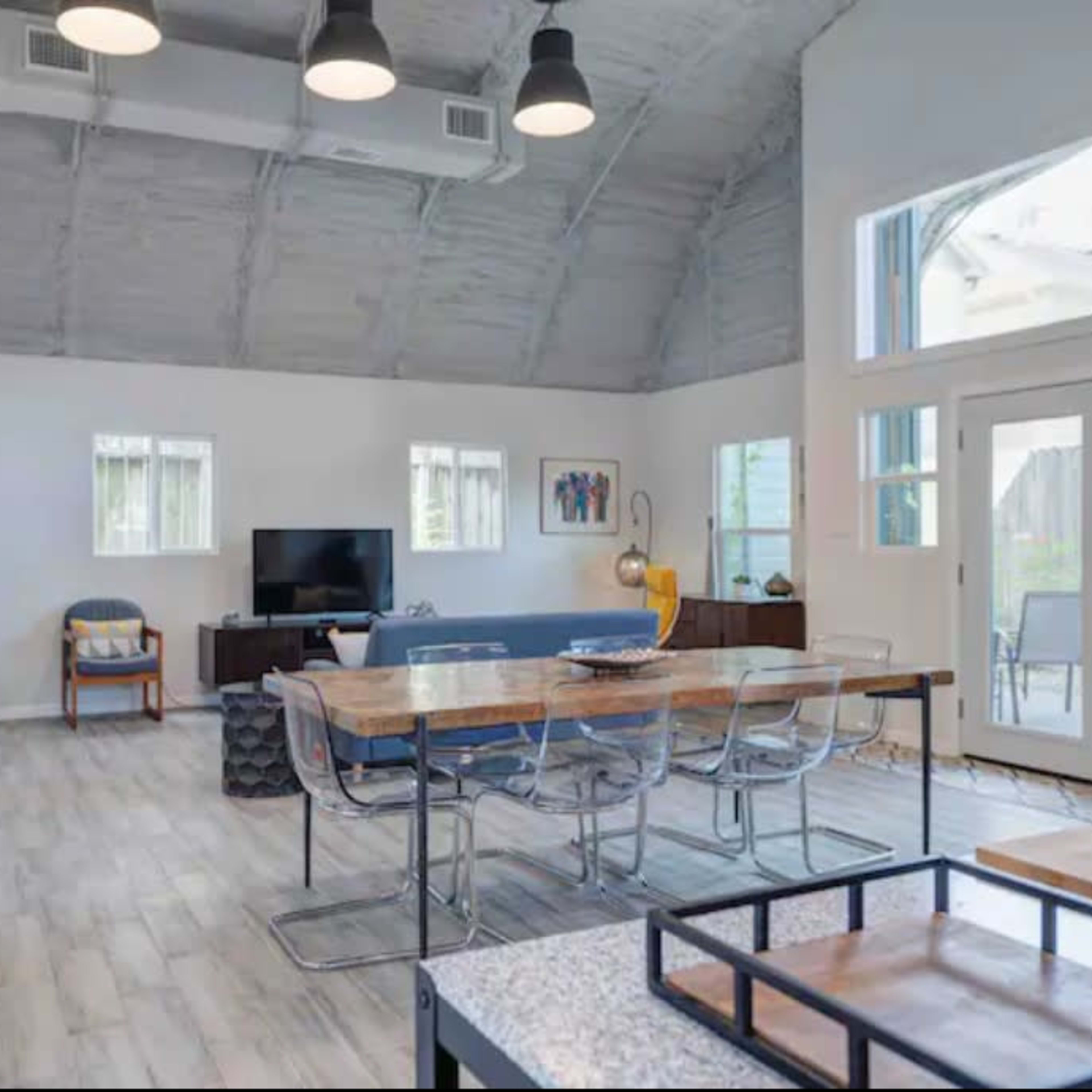 A spacious, modern living area featuring a large dining table, a television, and large windows that provide natural light.